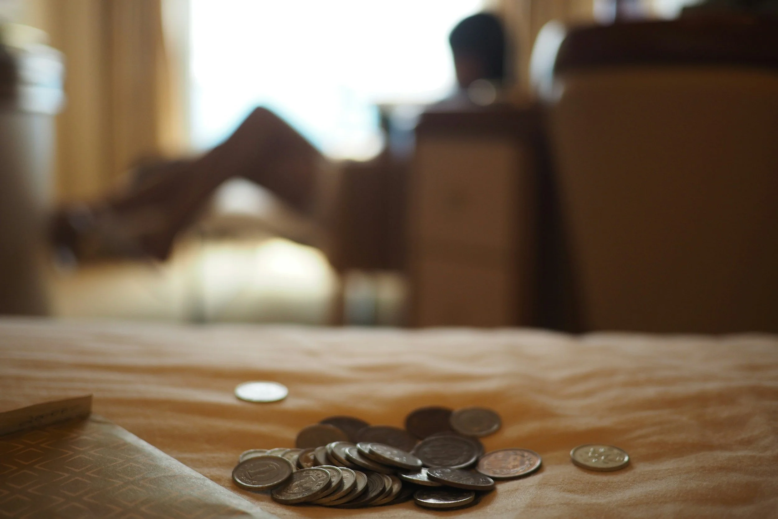 Coins scattered on a wooden surface with a blurred background of a person sitting at a desk or table.