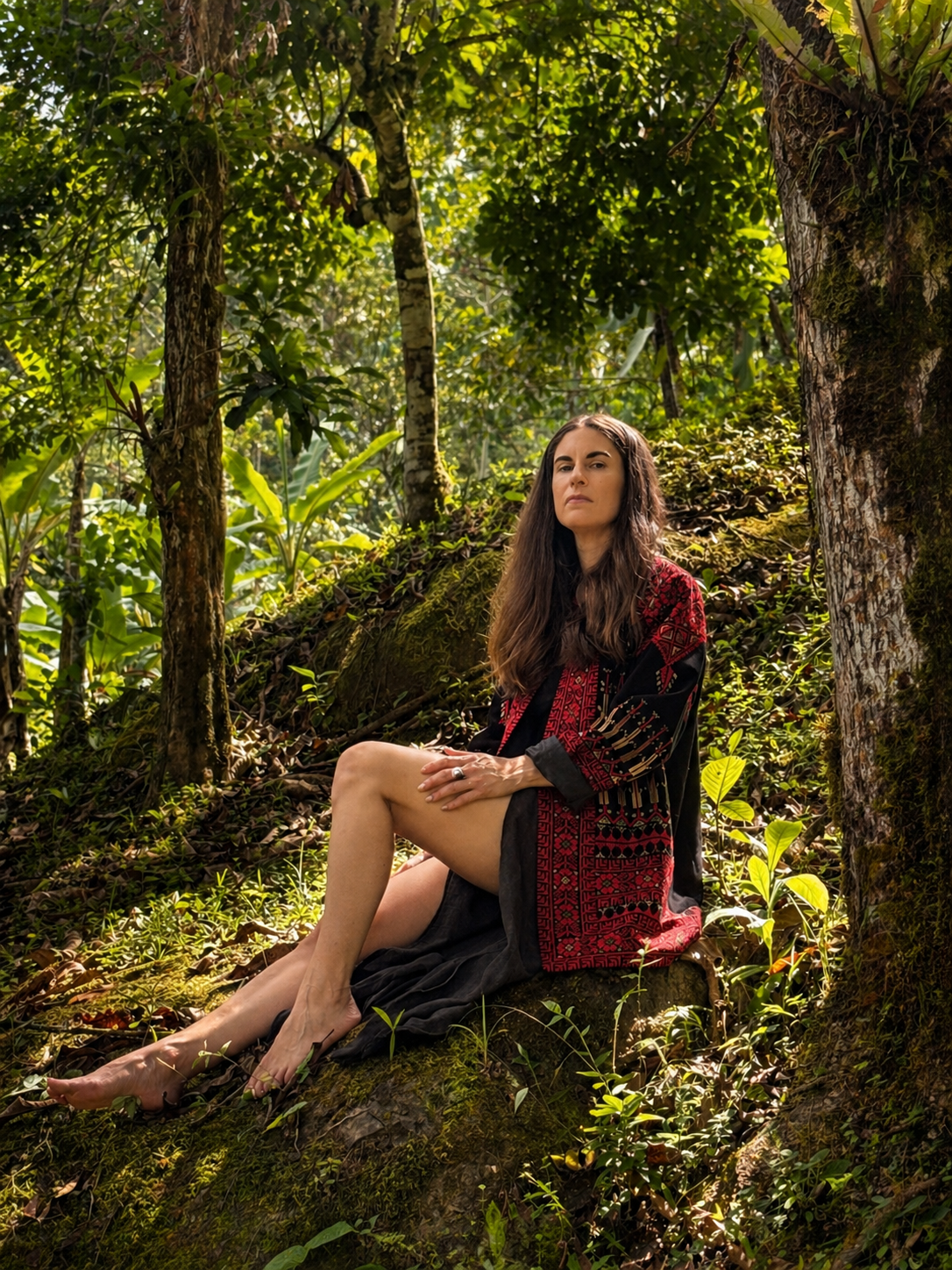 Amanda Elemental sitting on a moss-covered tree trunk in a lush green forest.