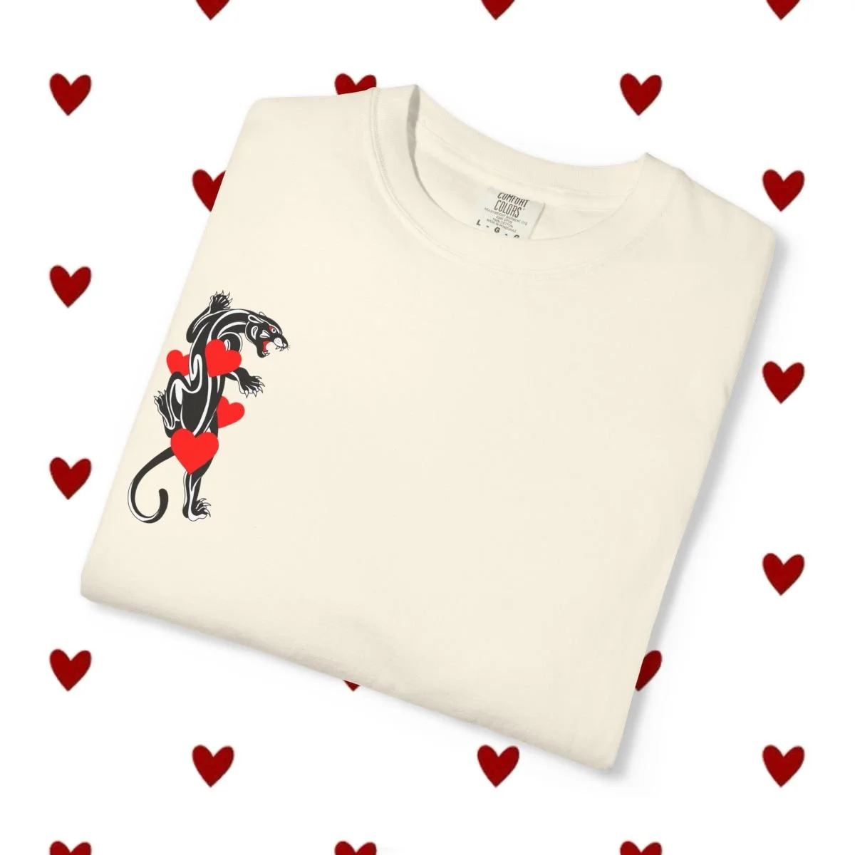 A white folded t-shirt with a graphic of a panther and red hearts on the left side, surrounded by a background pattern of small red hearts.