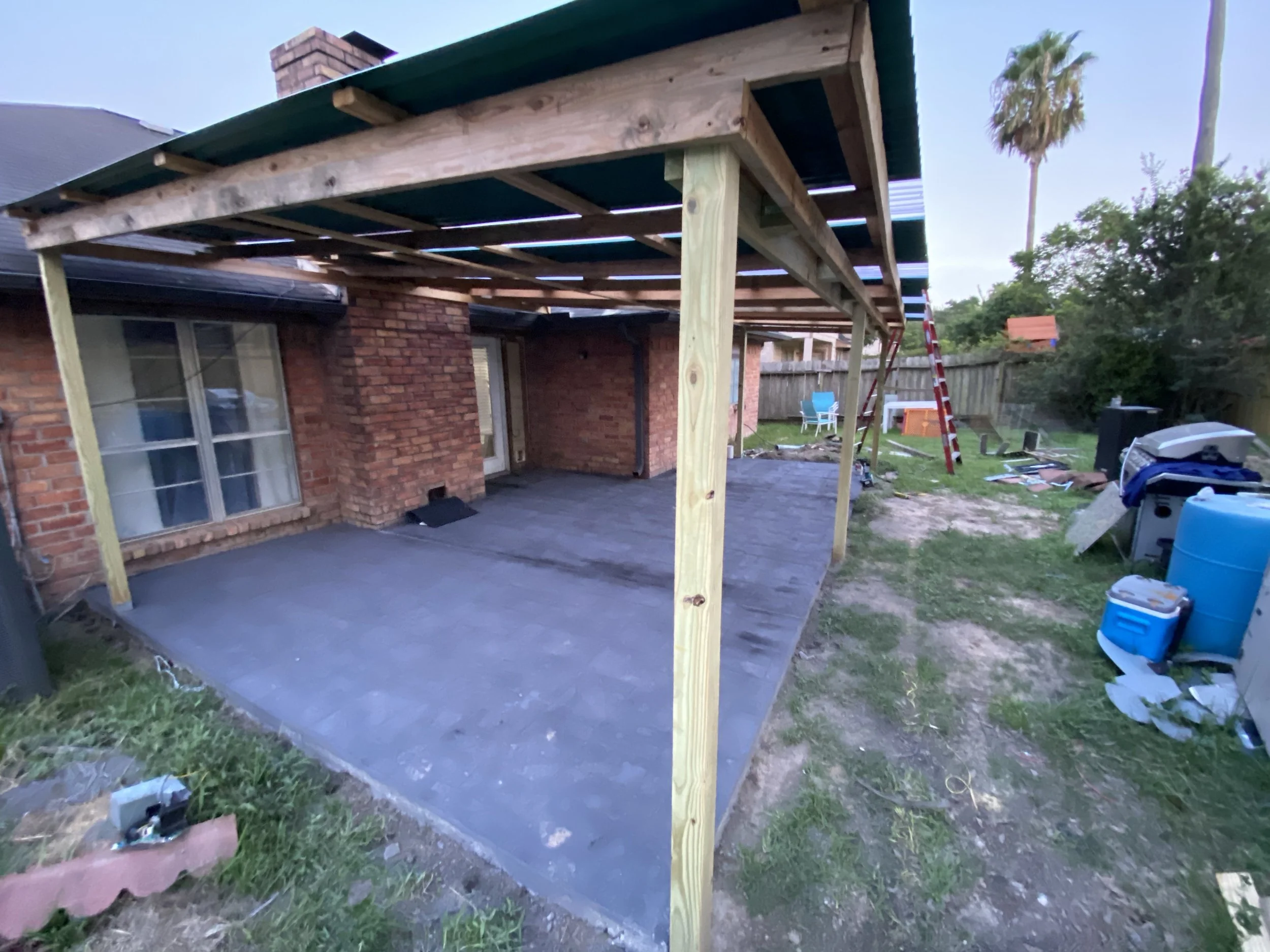 Construction of a wooden porch extension on the backyard of a brick house, with tools and materials scattered around.