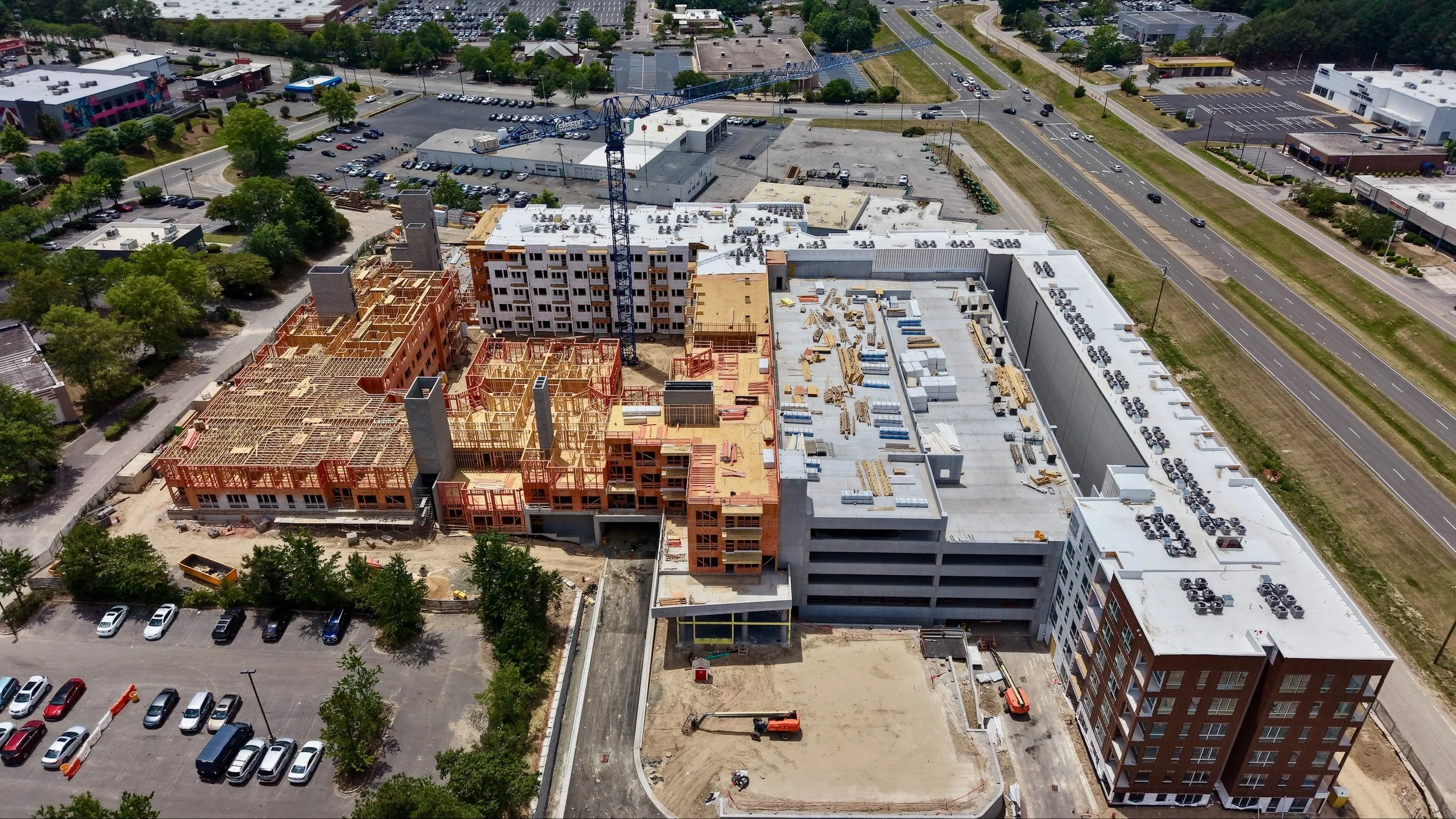 Aerial view of a construction site with buildings under development, a crane, and surrounding streets with parked and moving cars.