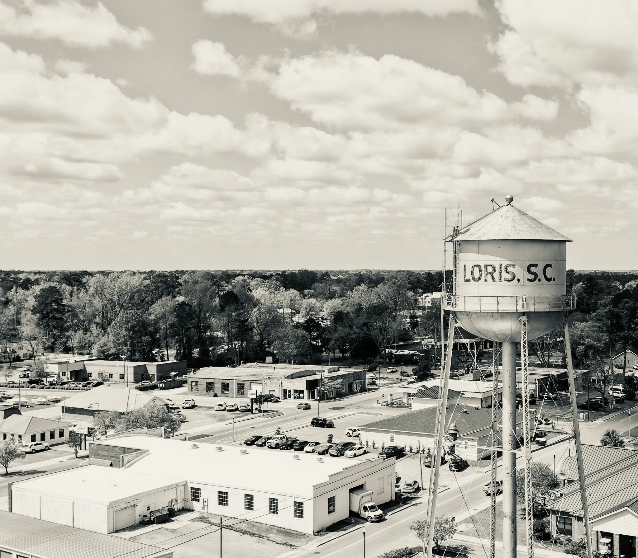 A water tower labeled 'Loris, S.C.' stands on the right side of the image. The background features a wide, open sky with scattered clouds and a expansive view of trees and buildings below.