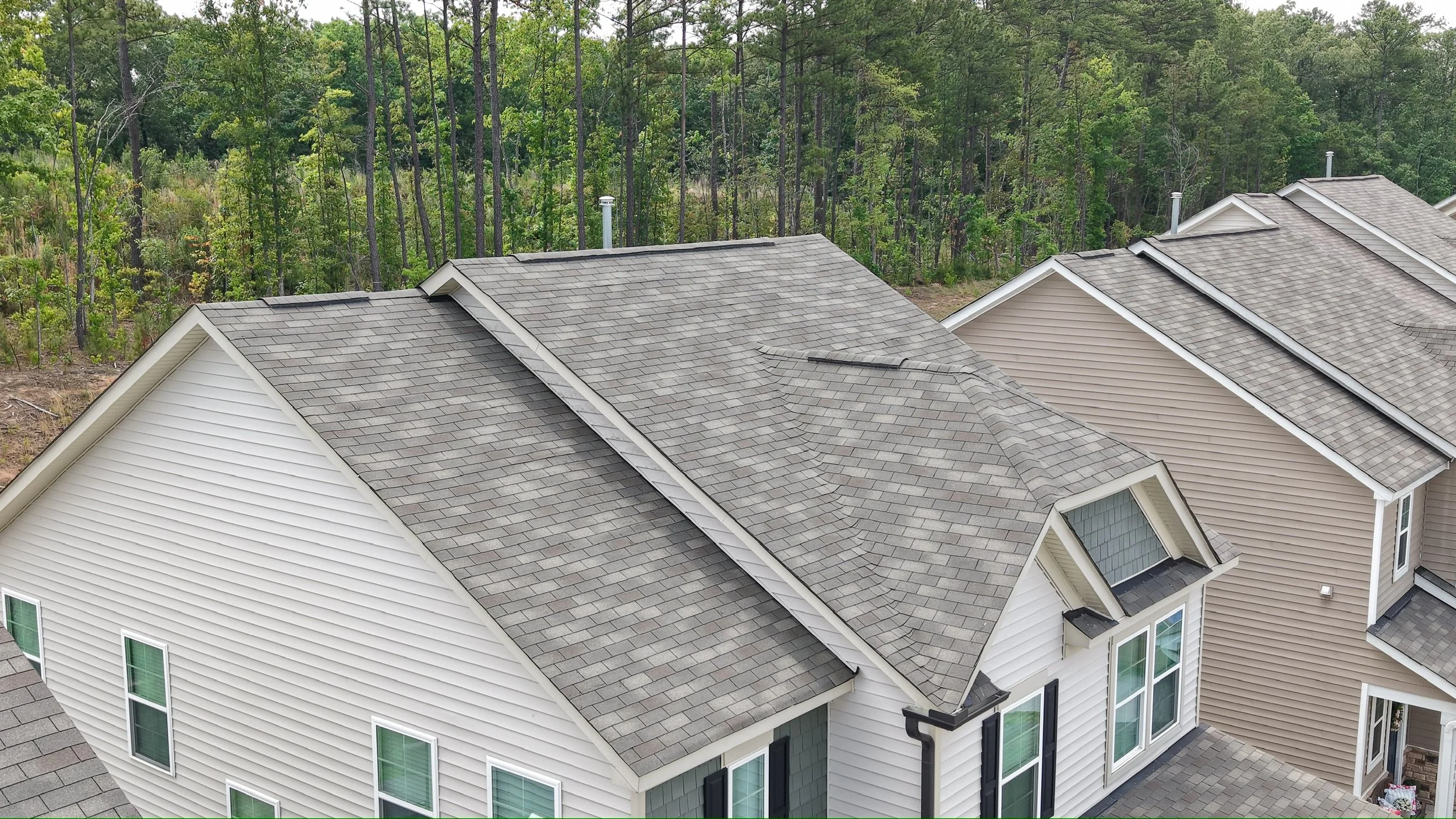 An aerial view of beige houses with gray shingle roofs, set against a backdrop of green trees.
