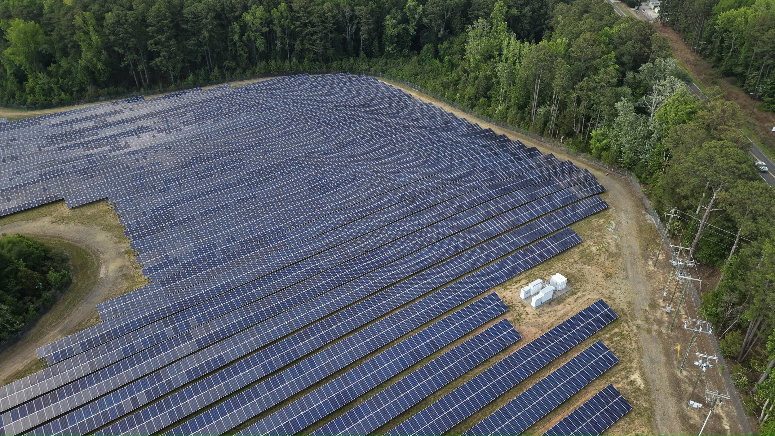 Aerial view of a large solar panel farm surrounded by trees and vegetation.