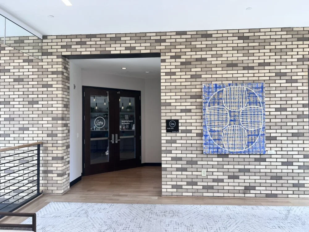 Interior of a modern building with brick walls, glass double doors, and a large blue abstract artwork on the wall.