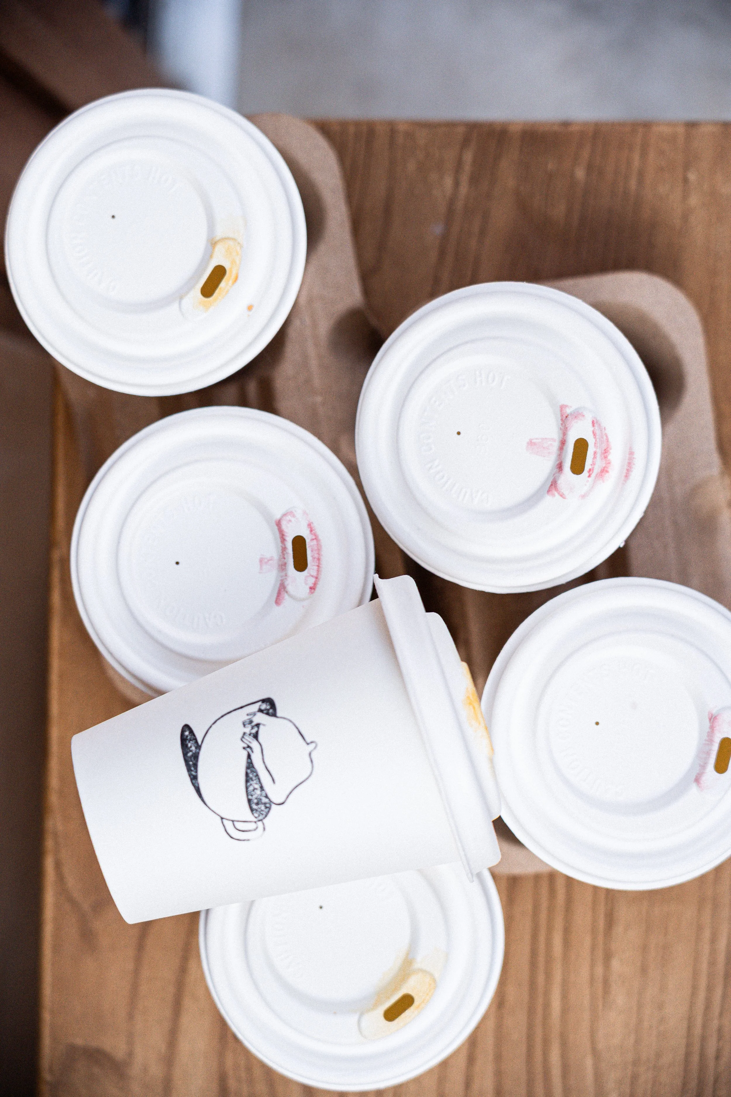 Cinq tasses en carton avec couvercles blanches posées sur une table en bois.