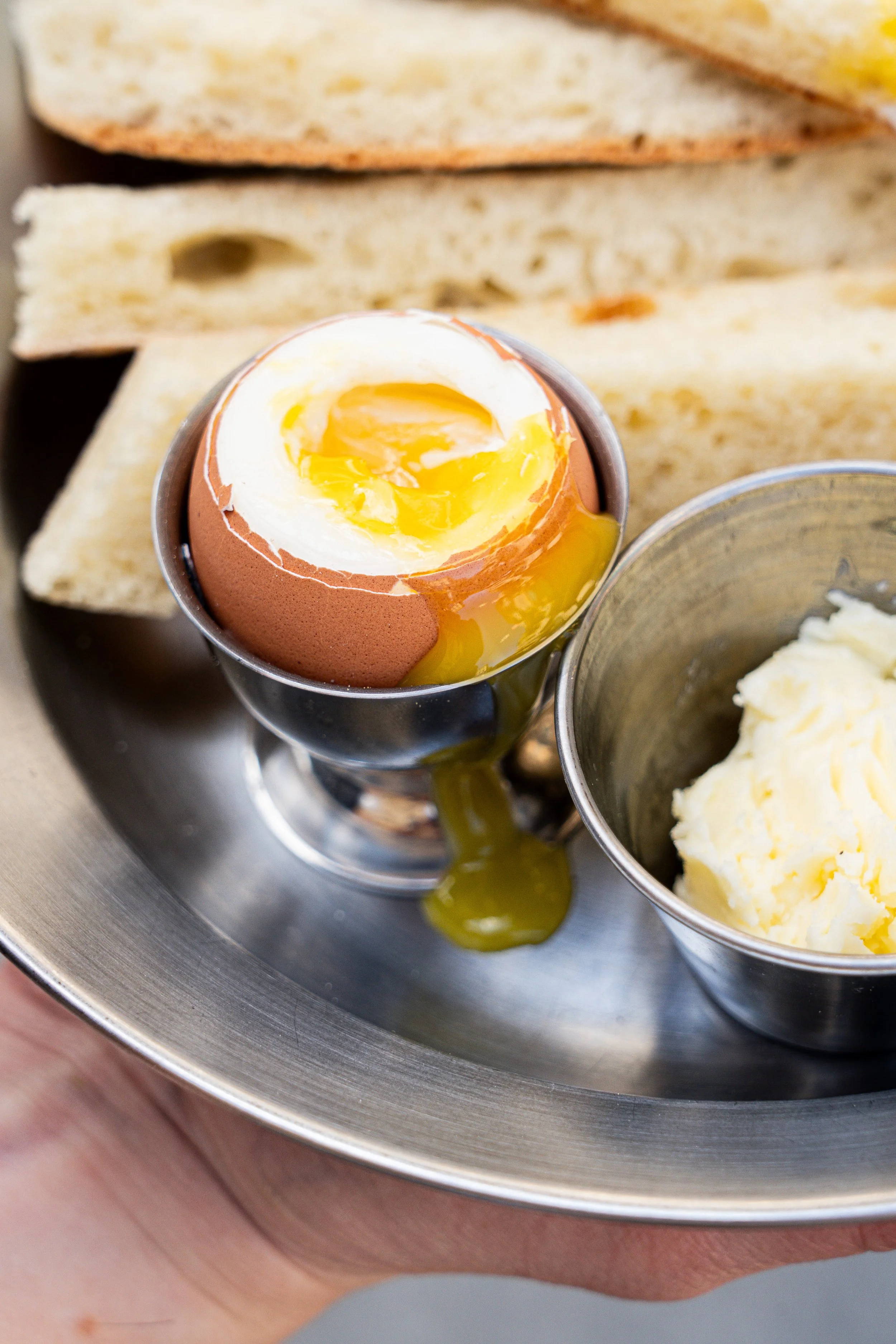 Oeuf à la coque, avec du jaune d'œuf encore liquide et du blanc d'œuf cuit, entouré de morceaux de pain beurré et de comté.