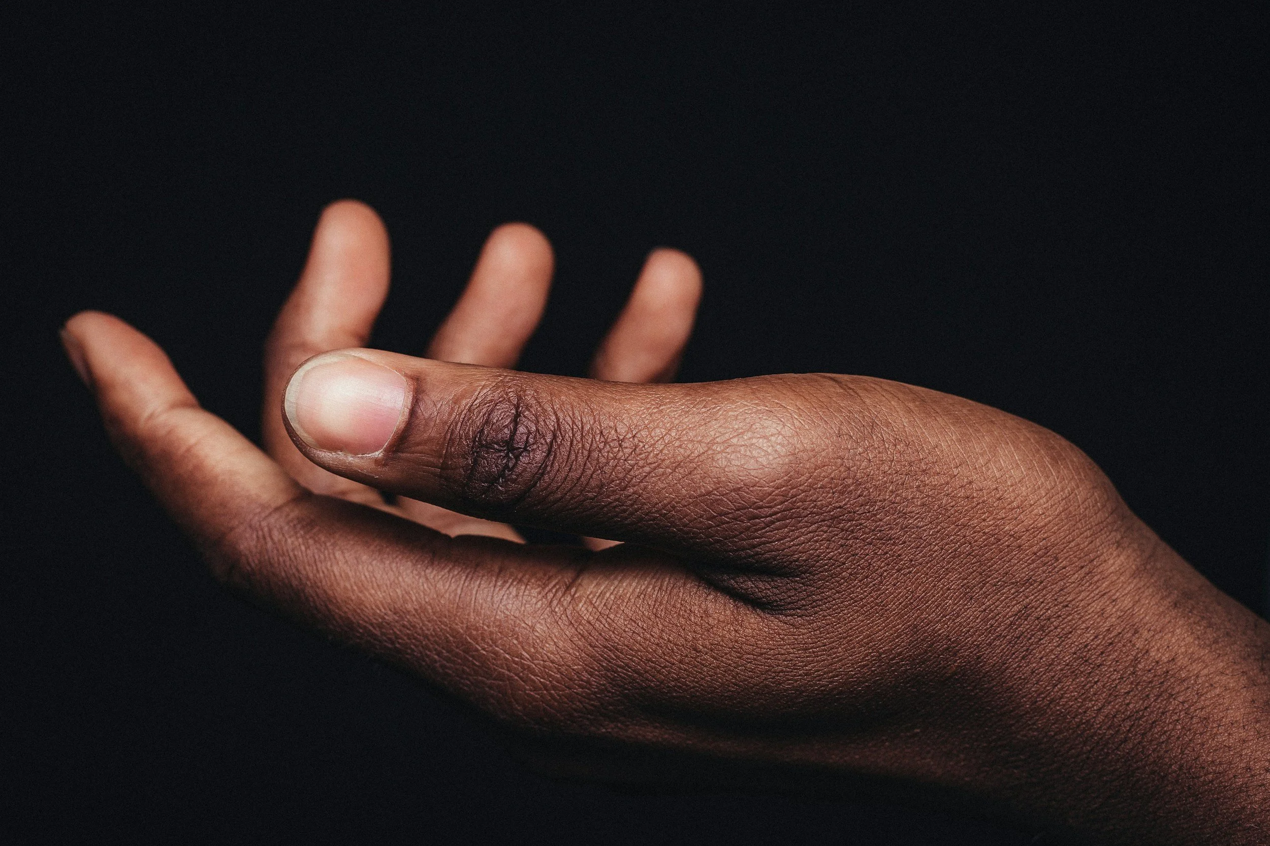 Close-up of a person's hand with dark skin, fingers slightly flexed, against a black background.