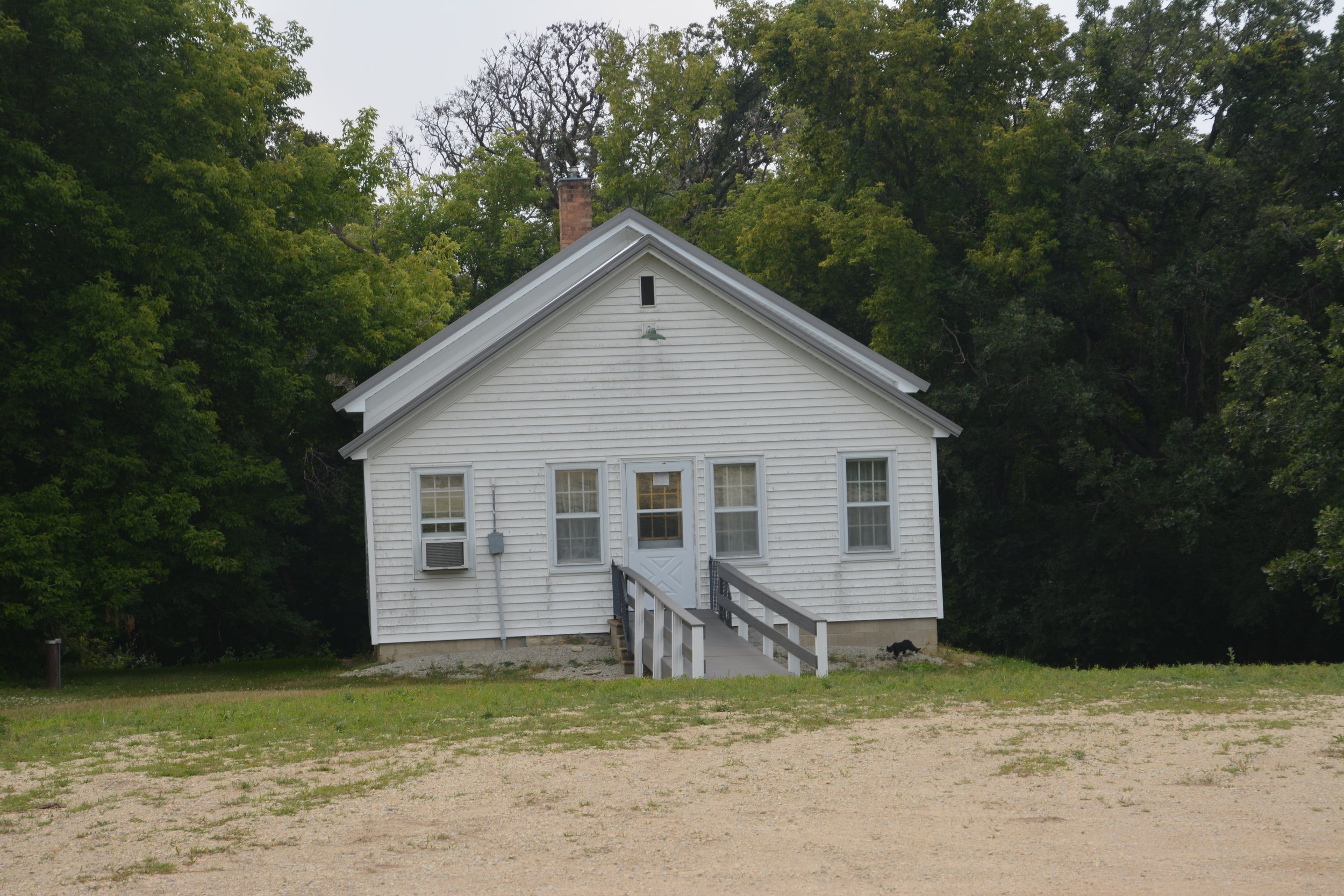 White house with a ramp leading to the front door, surrounded by green trees and a grassy area.