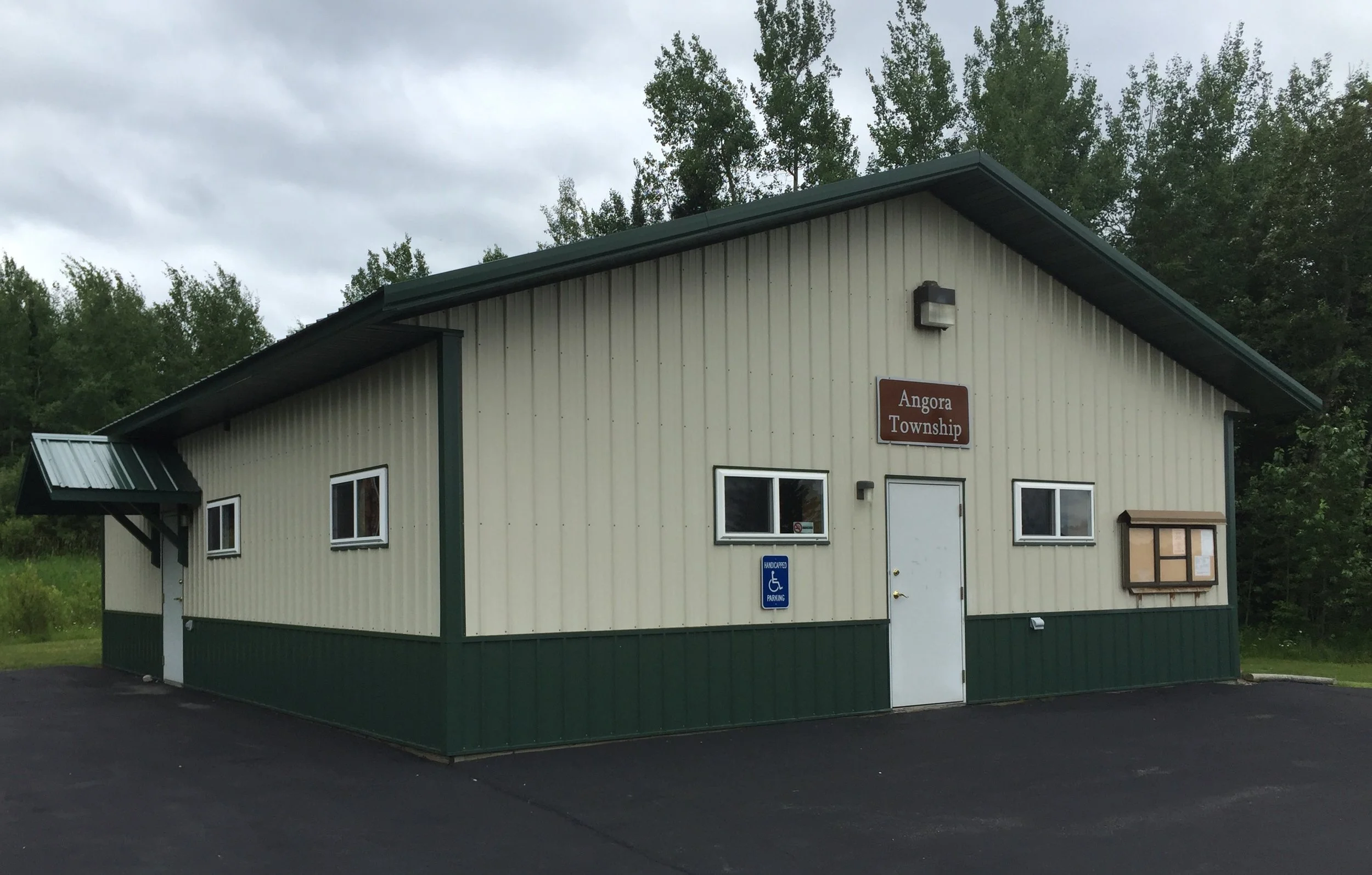 A beige and green building with a sign that reads 'Angora Township,' surrounded by trees and overcast sky.