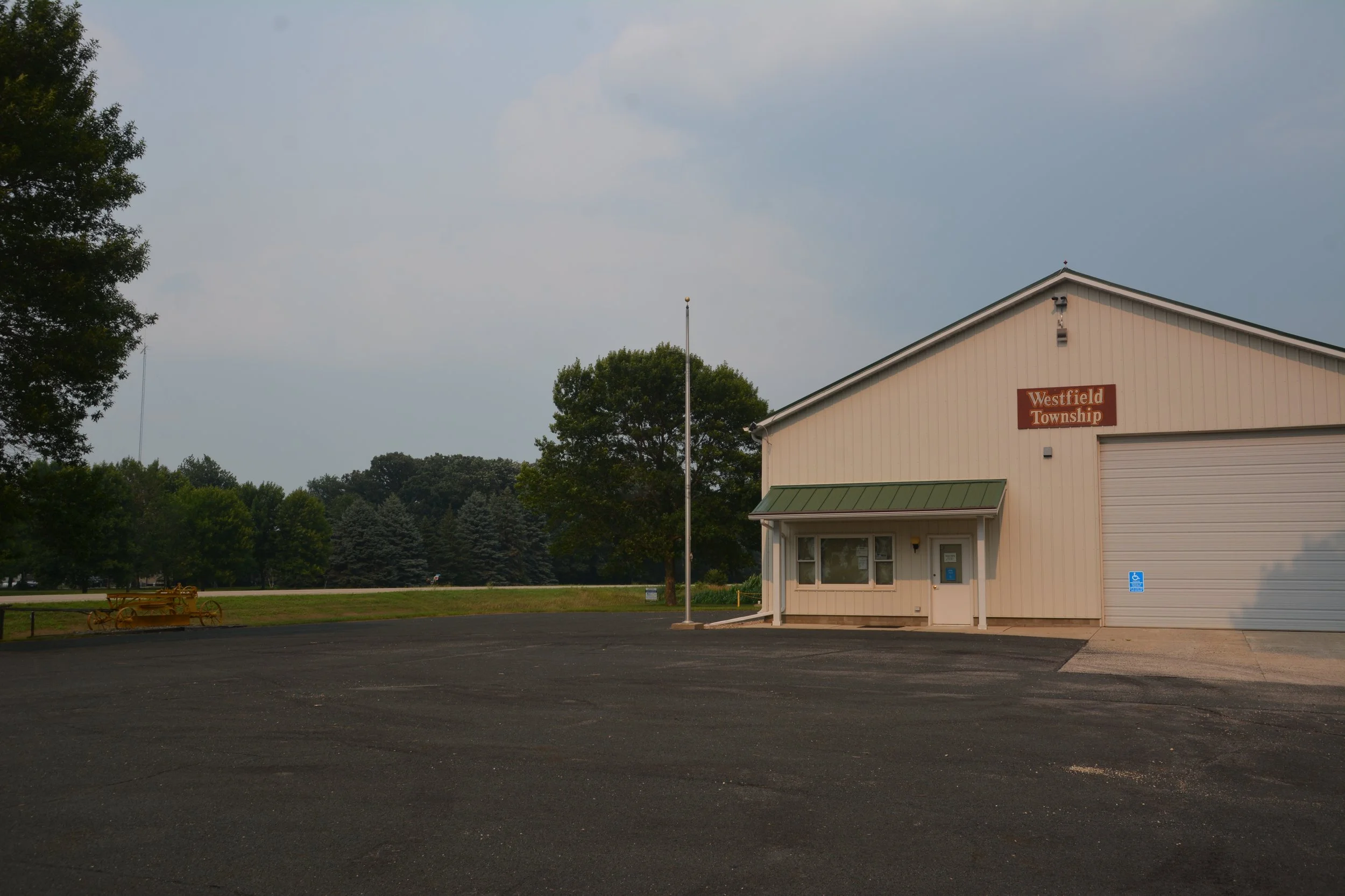 A beige building with a sign that reads 'Westfield Township,' a small porch, and a traffic handicap parking space in front. Surrounding trees and a cloudy sky.