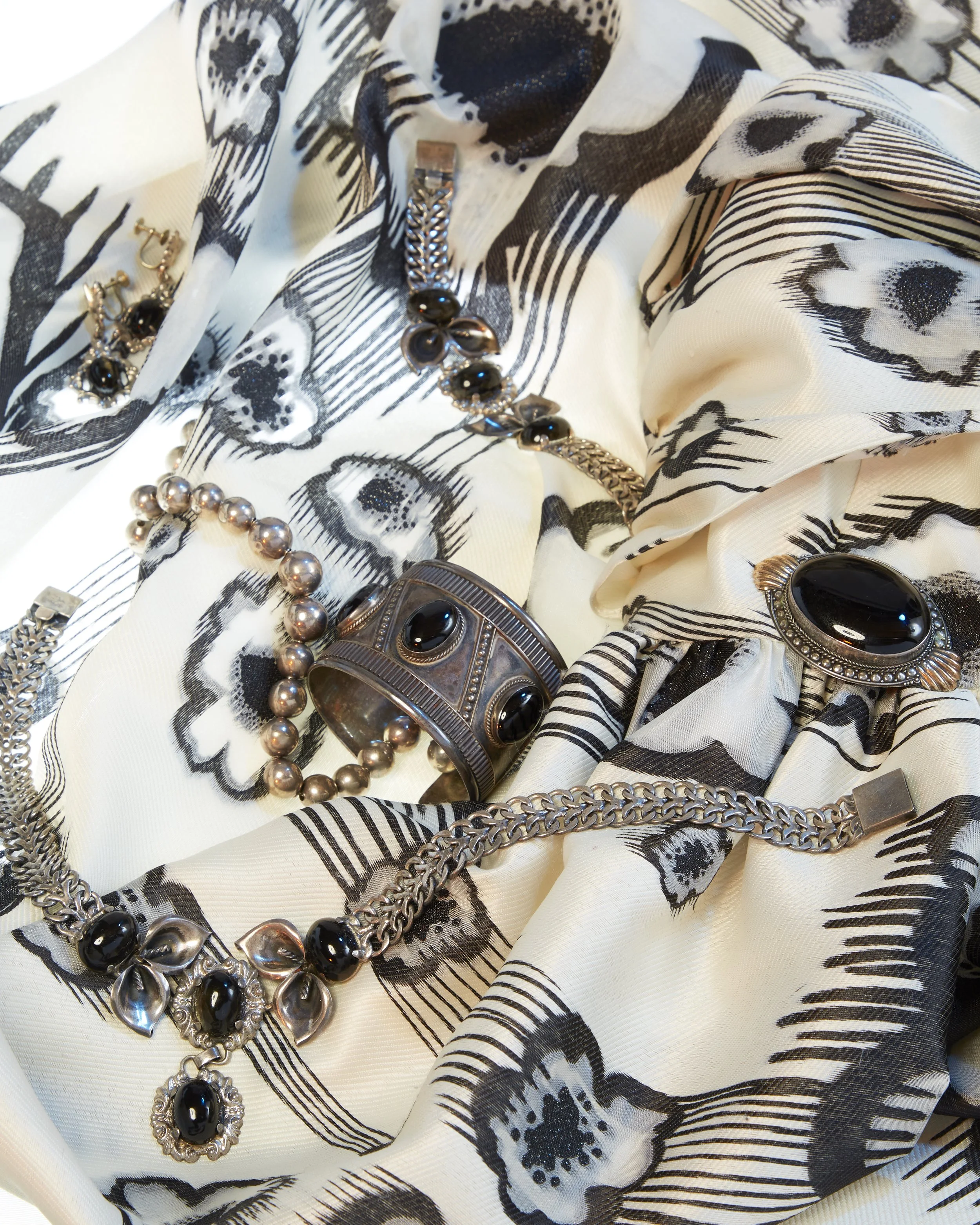 Various pieces of jewelry, including necklaces, bracelets, and earrings, displayed on a black and white patterned fabric with large eye and face designs. jewelry photography and jeweler specialization