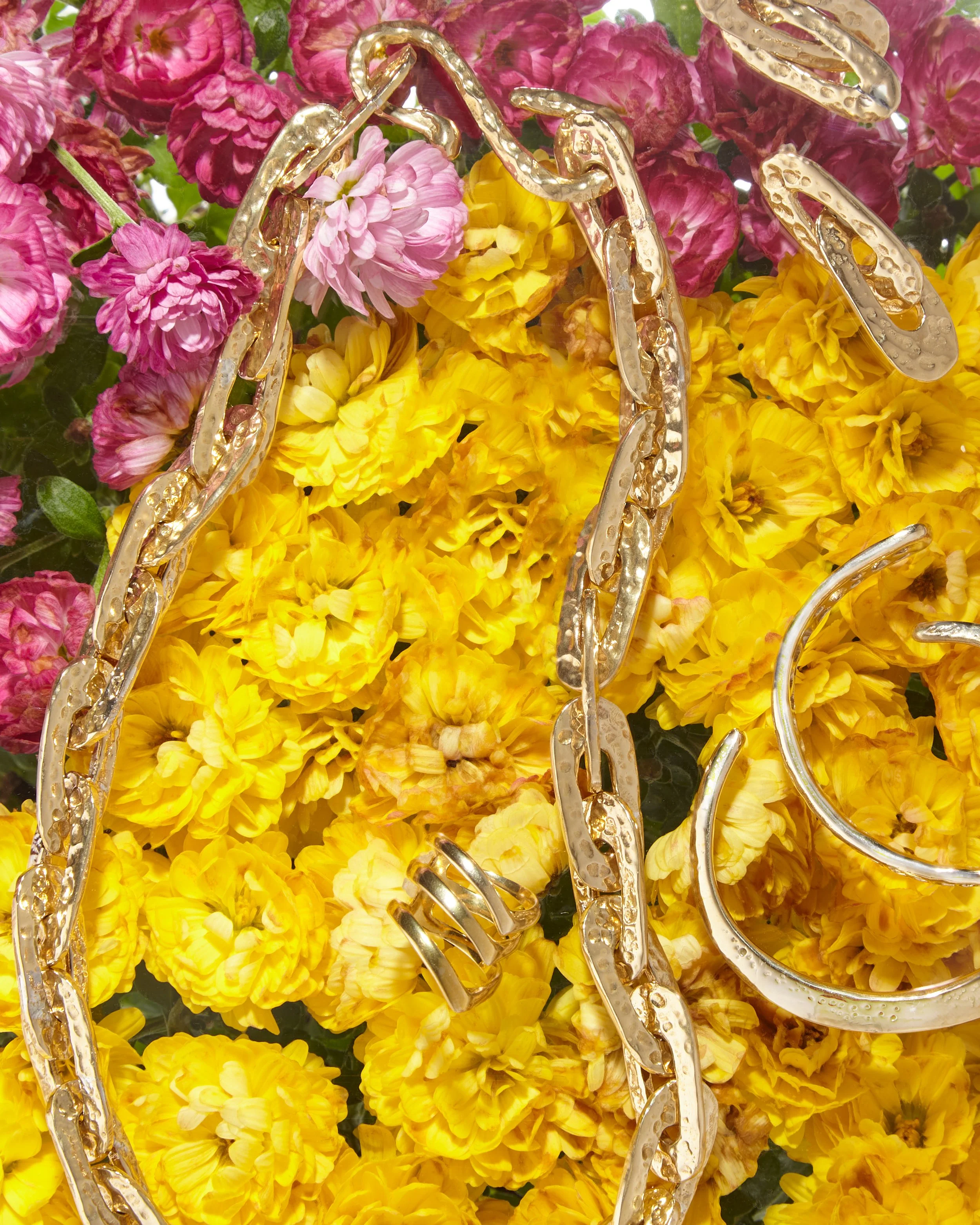 Close-up of gold jewelry, including chains and earrings, placed on a bed of pink, yellow, and purple flowers. propping and still life photography