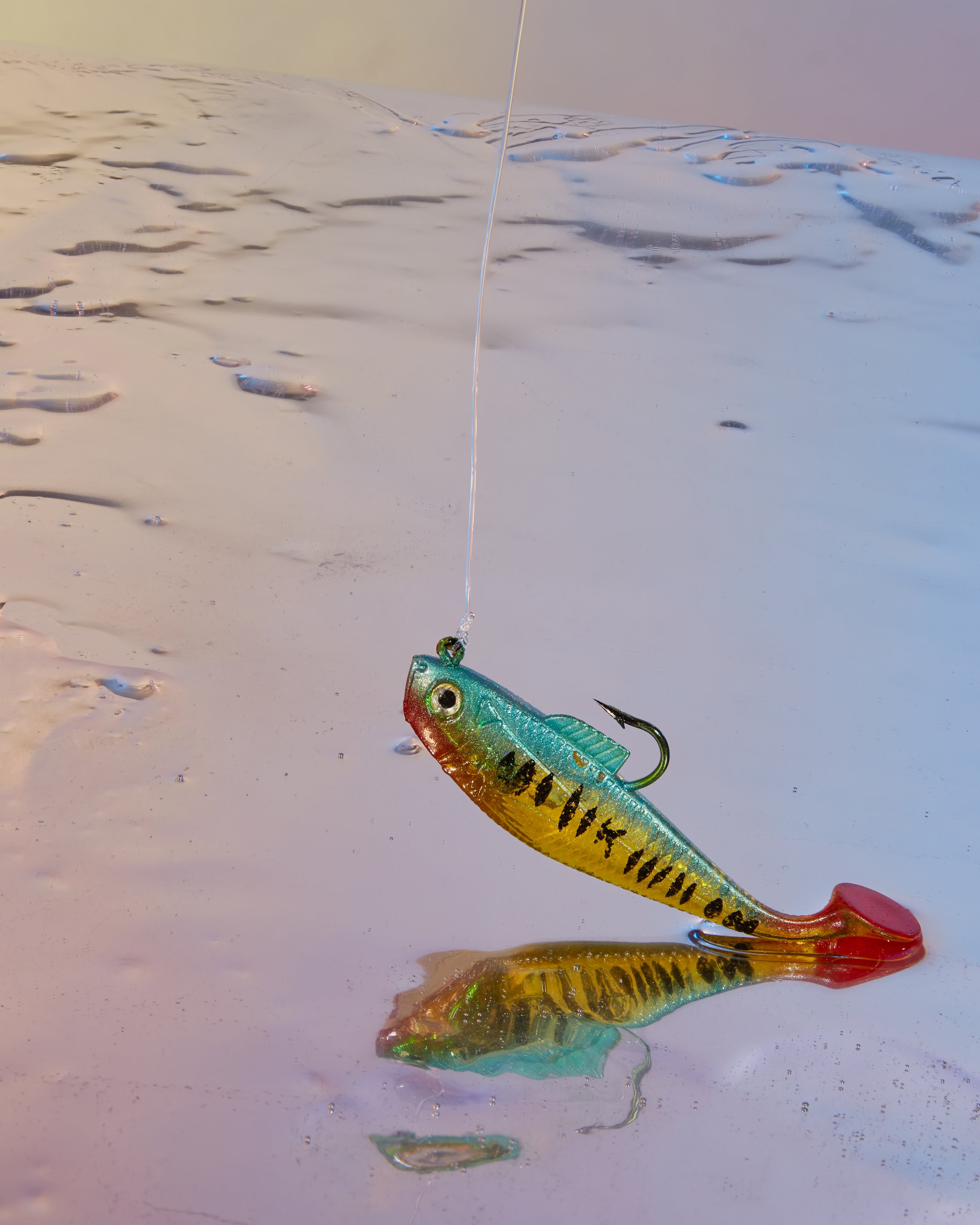Colorful fishing lure with a fish design hanging above water, casting a reflection. Creative Concepting Rapala and Stike King for advertising editorial, advertorial by Gabe Weber and Hope Misterek, branding, image, aesthetic, creativity, photography,
