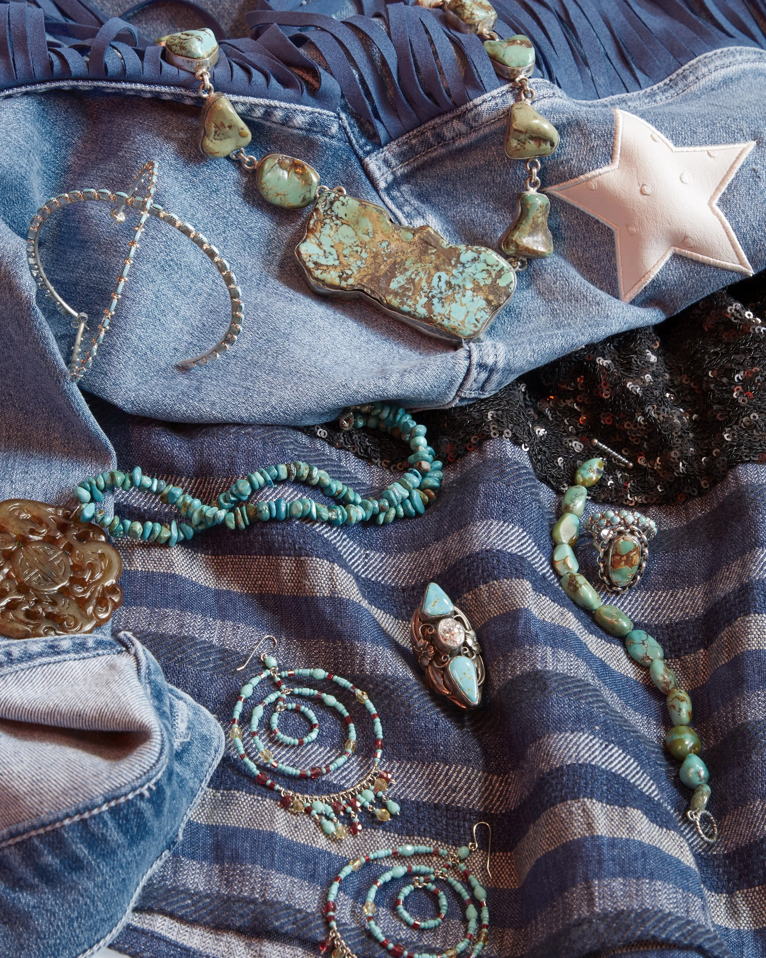 Various jewelry pieces, including turquoise and silver necklaces and rings, are displayed on a denim fabric background with a star patch and black sequined fabric. jewelry precious metals fine jewelry handling specialization