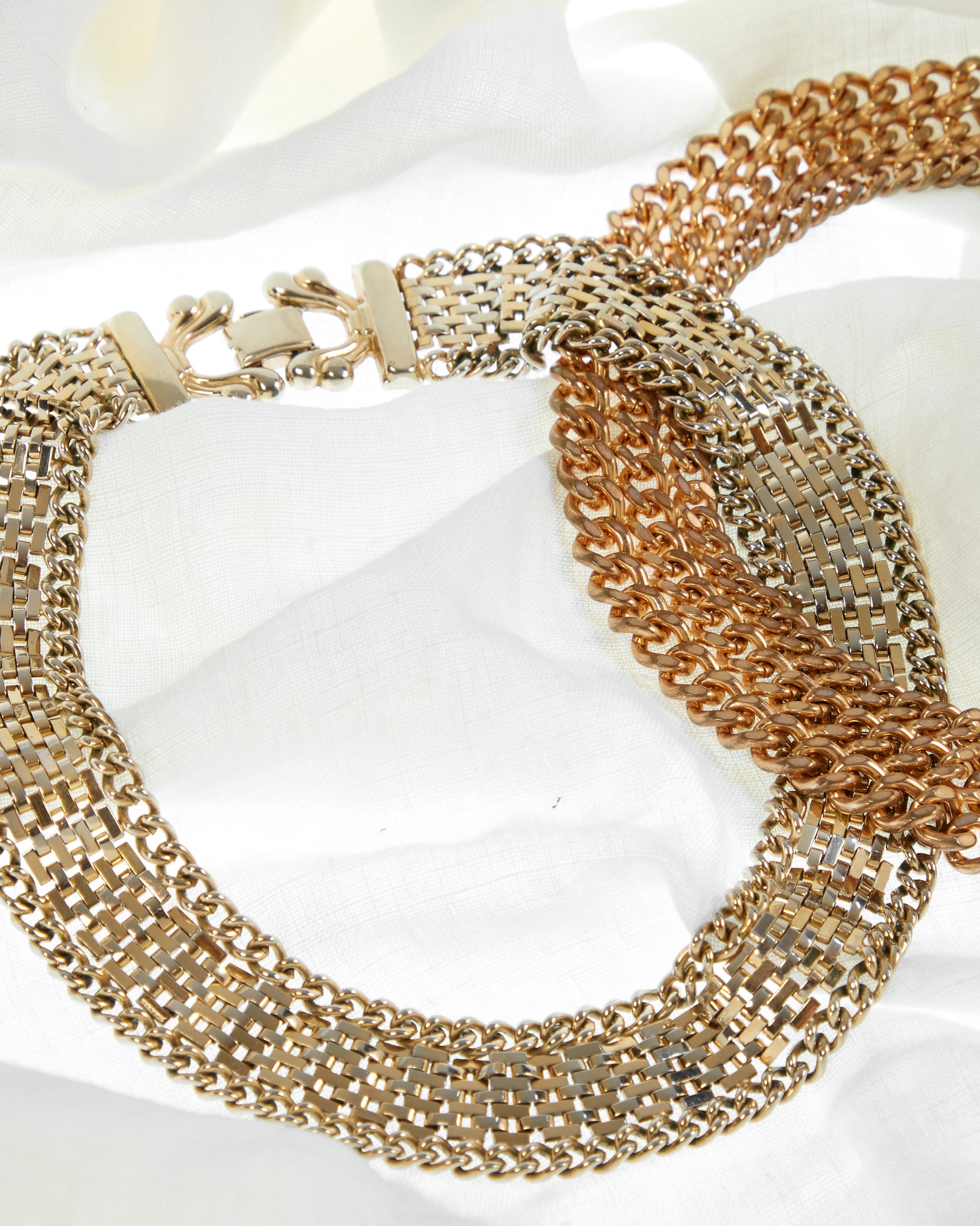 Multiple gold and silver metallic chain necklaces displayed on white fabric. jewelry photography specialization 