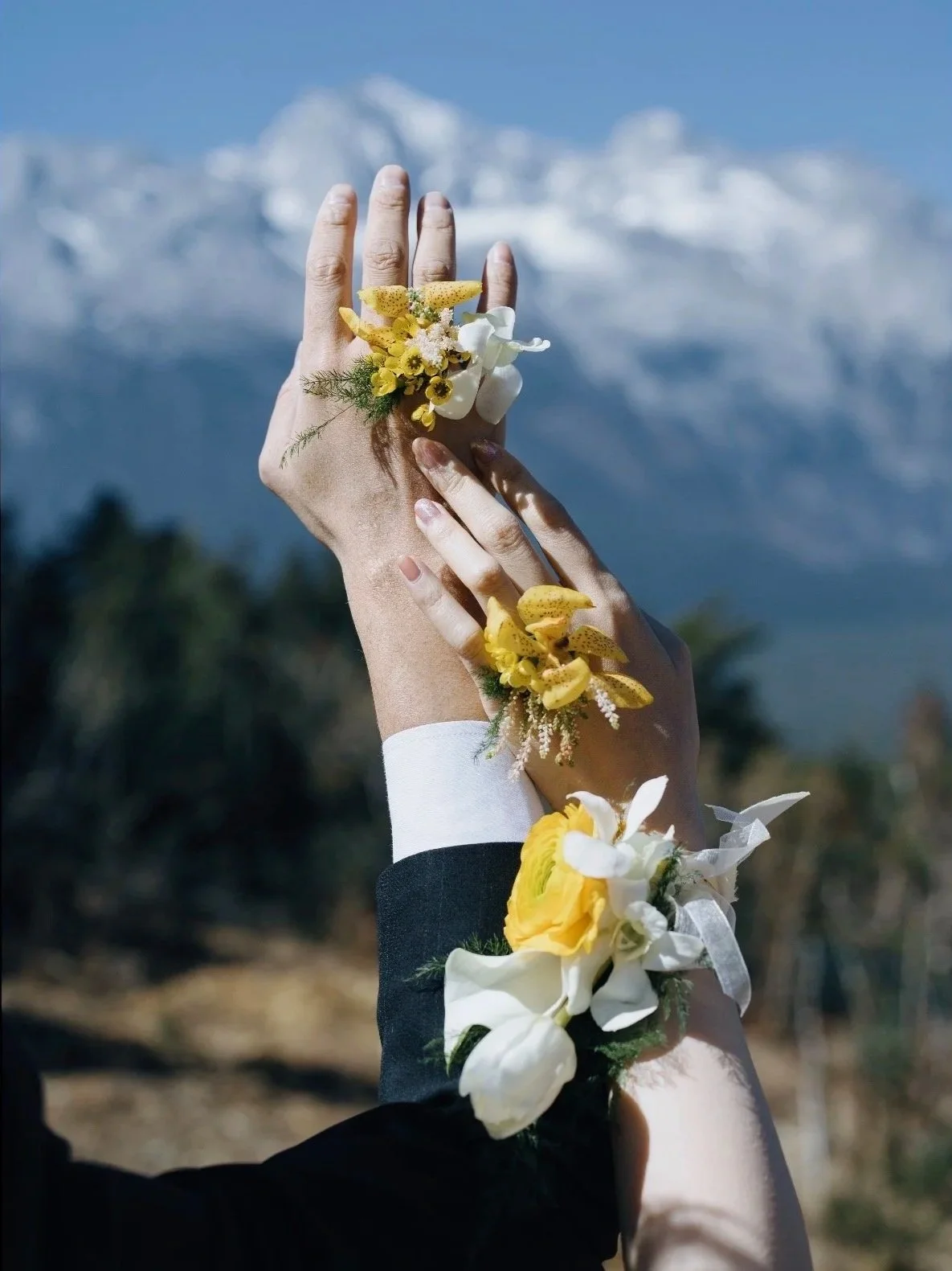 Hands of a bride and groom with floral cuffs, with a mountain landscape in the background.