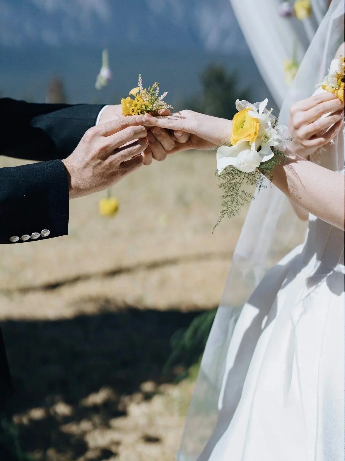 A couple during a wedding ceremony exchanging rings, with their hands and floral cuffs visible.