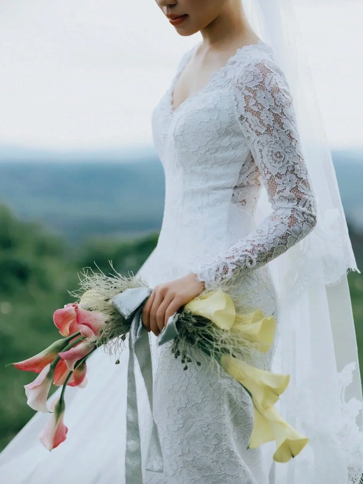 Bride in a white lace wedding dress holding a colorful bouquet outdoors.