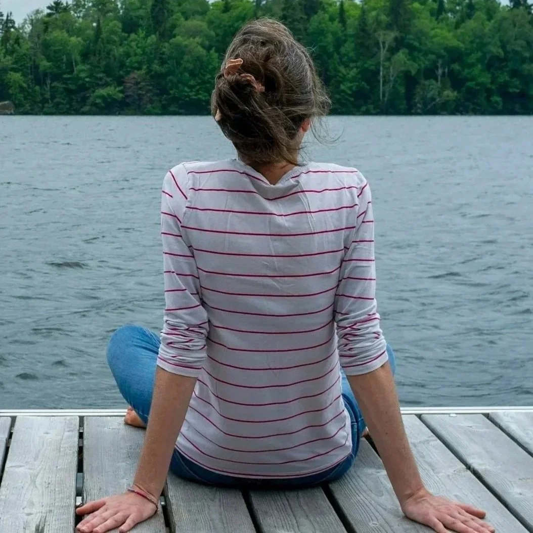 Woman sitting on a dock facing a lake surrounded by green trees