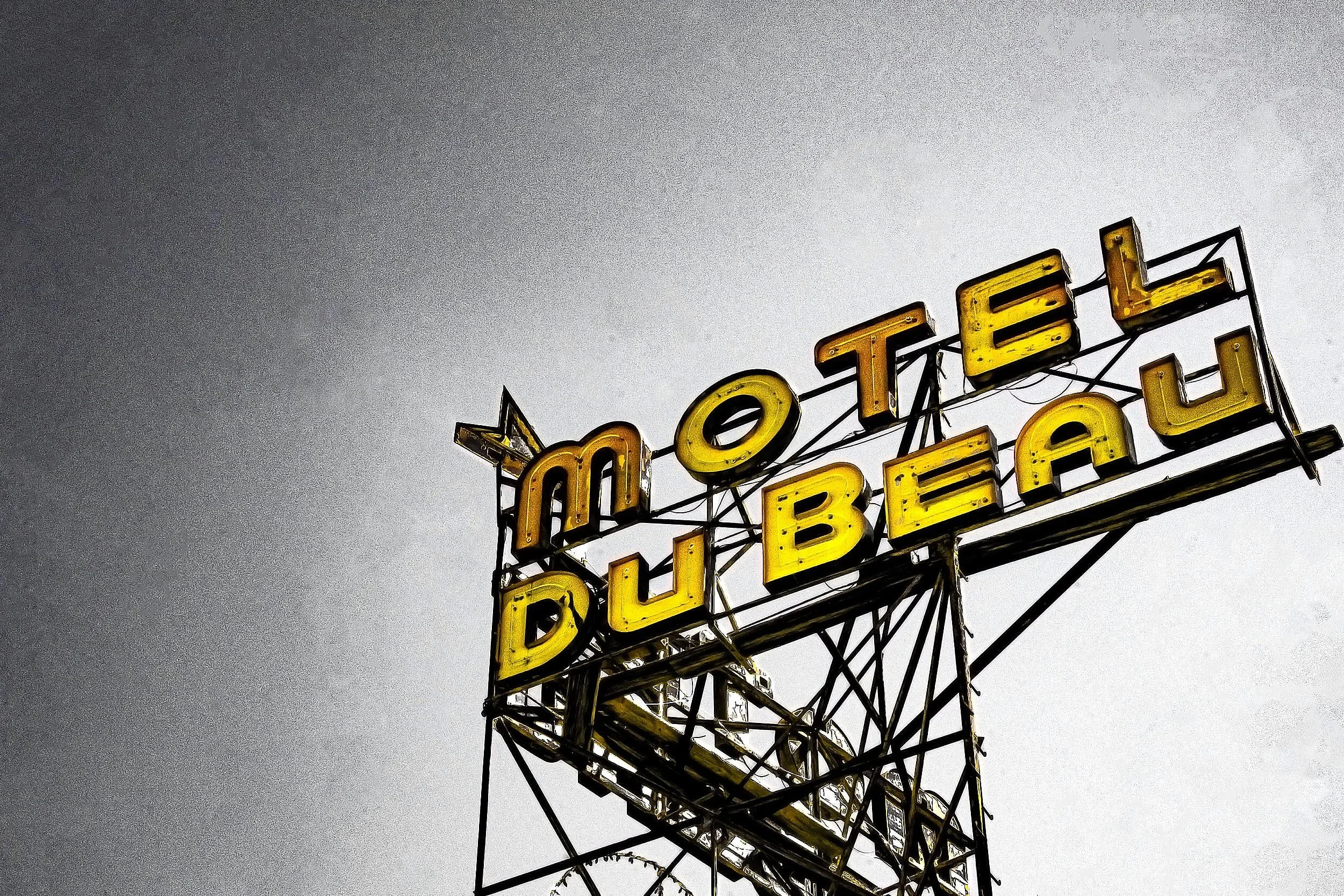 Close-up of an old, yellow neon sign that reads 'HOTEL' against a cloudy sky.
