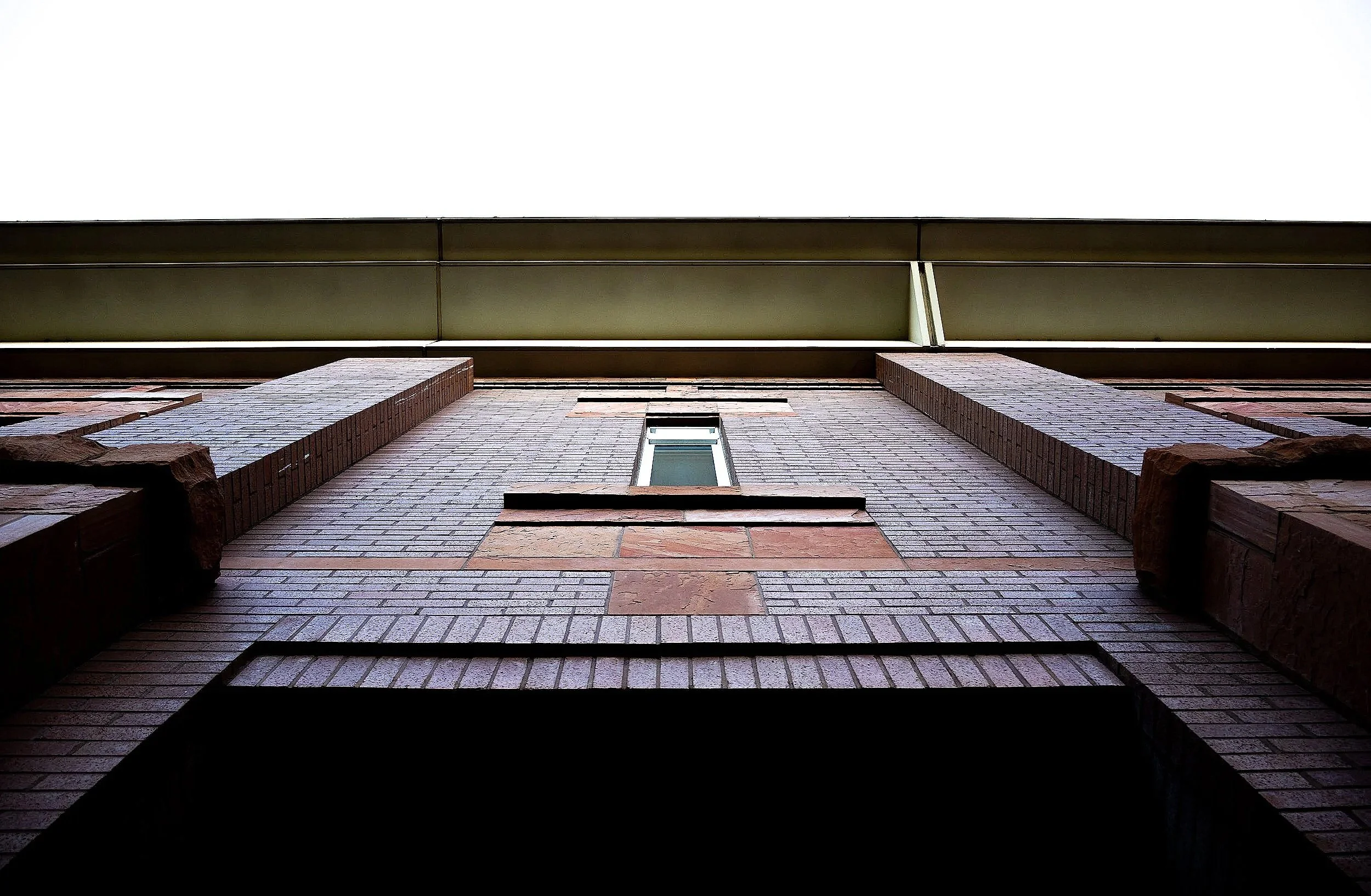 Looking up at a brick building with a small window and a metal overhang at the top.