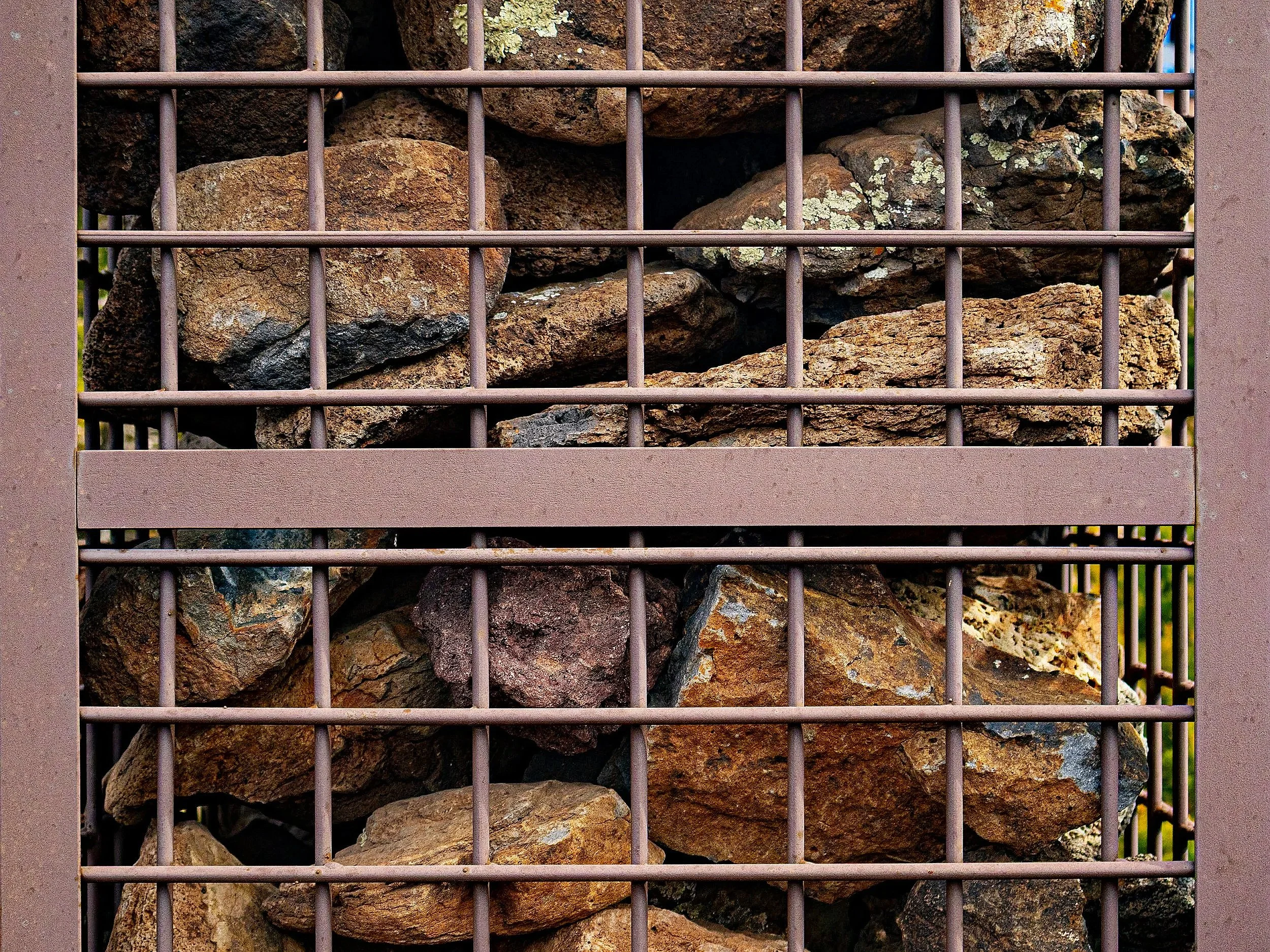 A metal grate filled with irregularly shaped rocks, with some lichen growing on them.