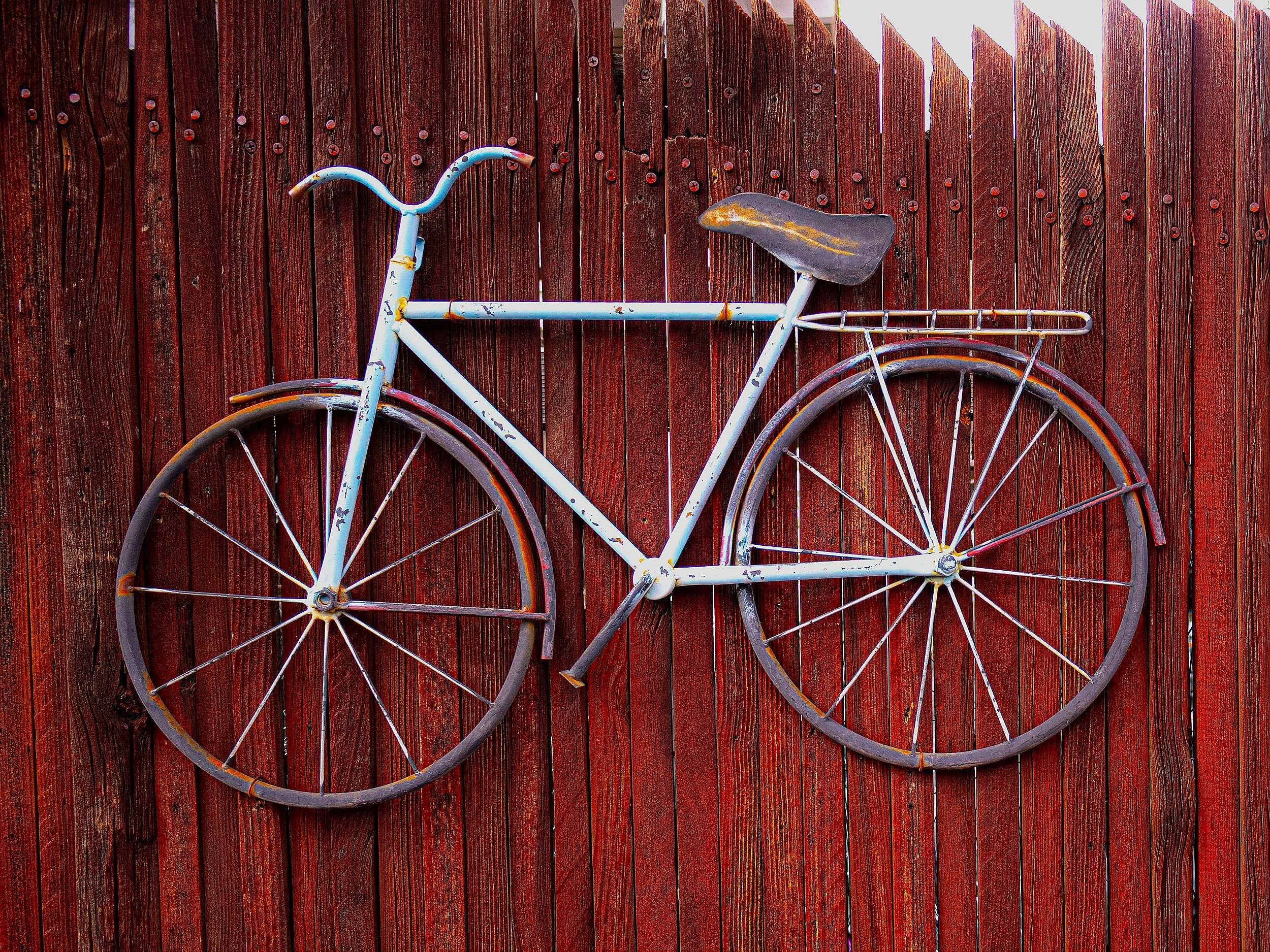 A vintage bicycle with rusted parts and a worn leather seat mounted on a red wooden fence.