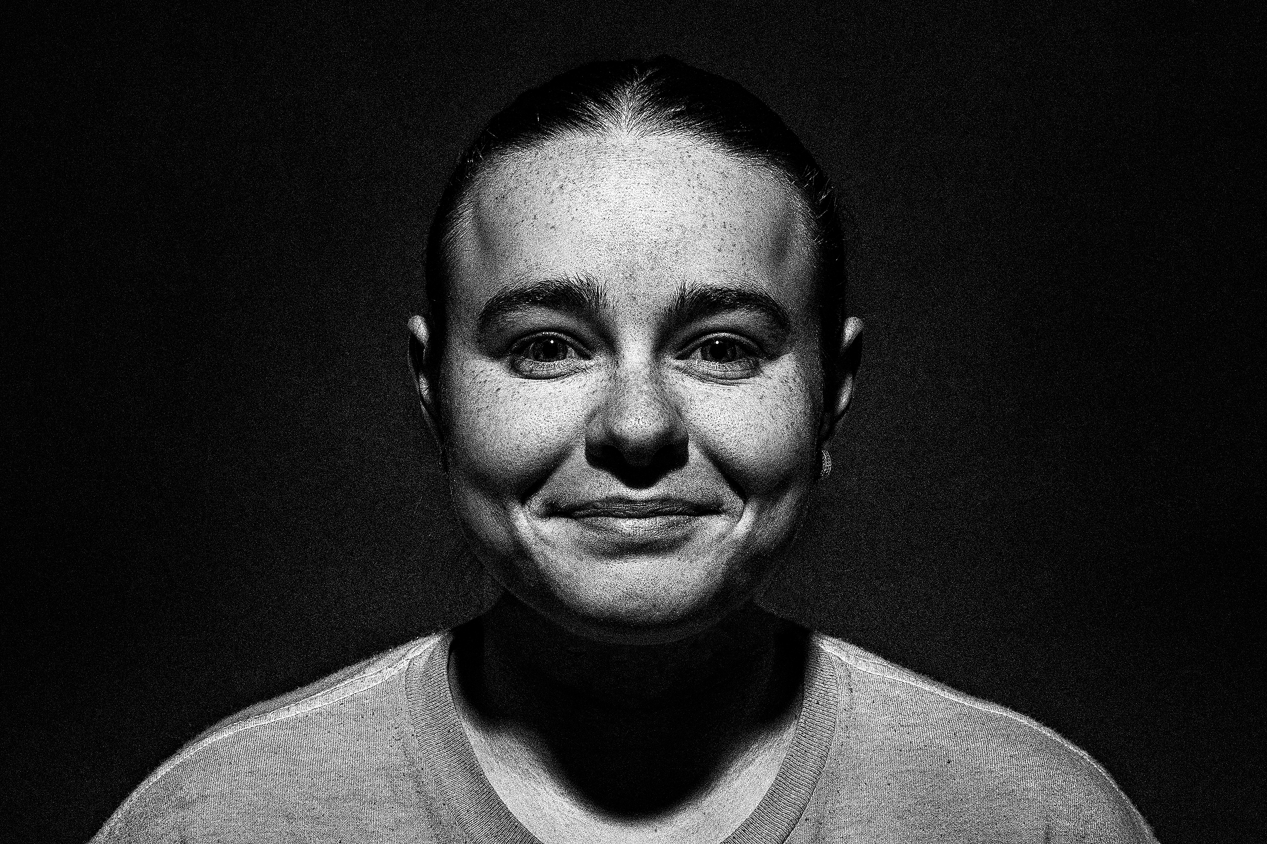 Black and white portrait of a smiling woman with smooth hair in a low bun, wearing a textured top.