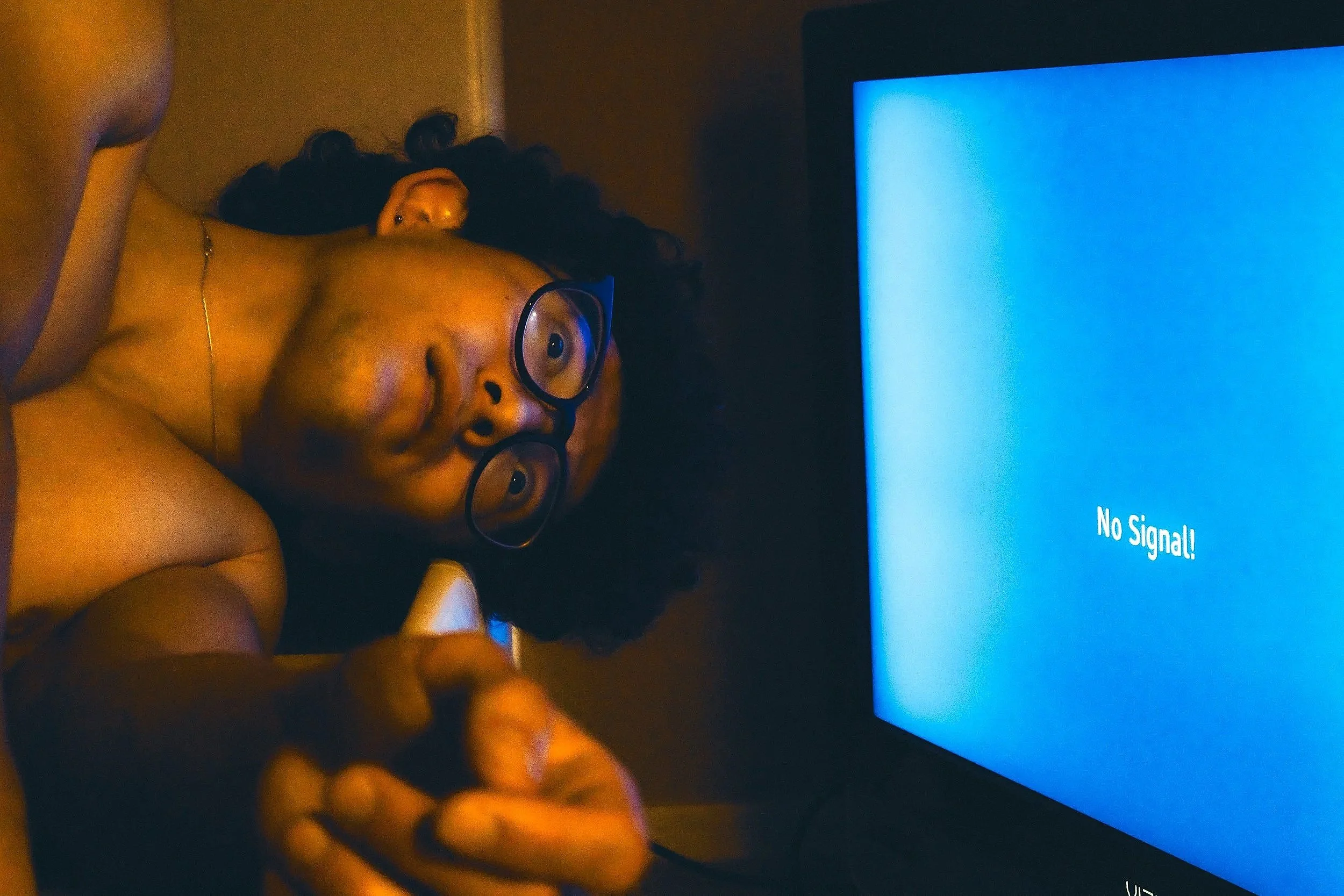 Person with glasses lying down beside a television with a blue screen displaying 'No Signal!'