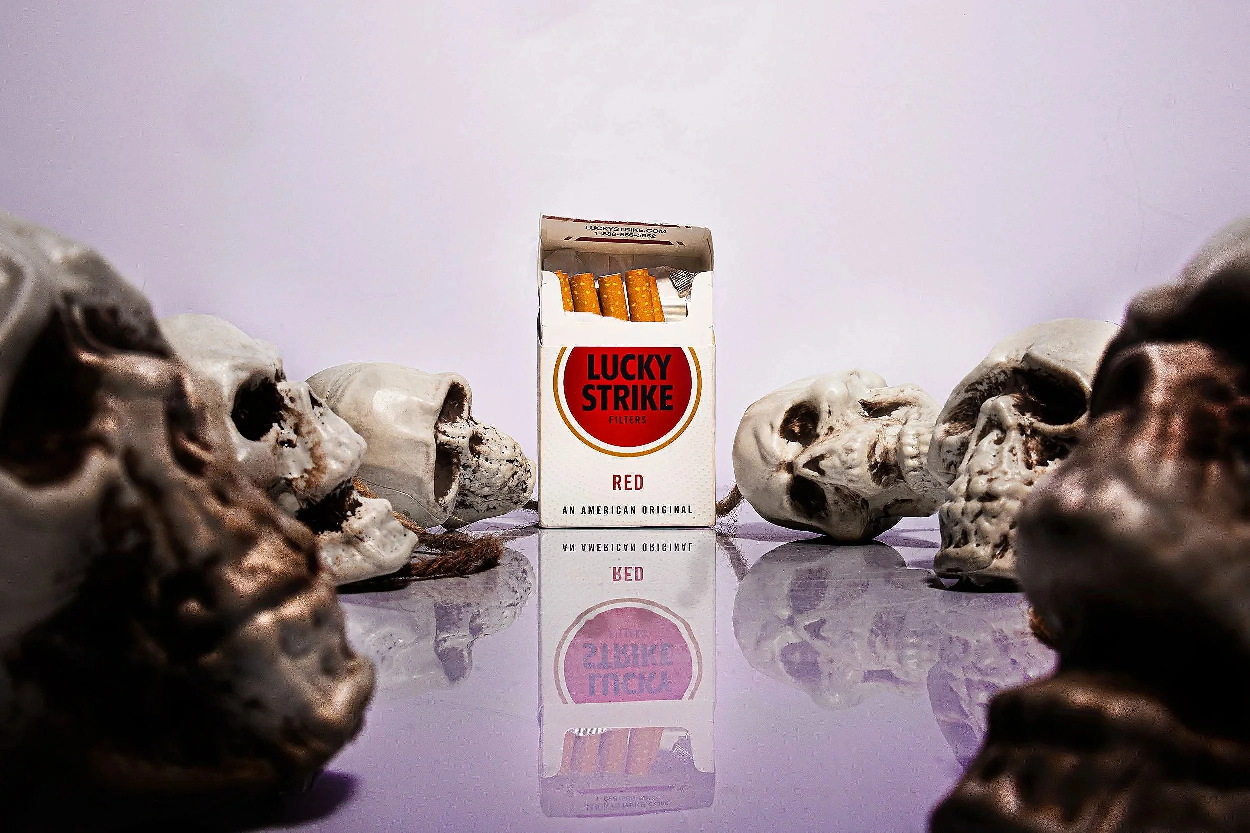 A pack of Lucky Strike red cigarettes surrounded by skulls on a reflective surface.