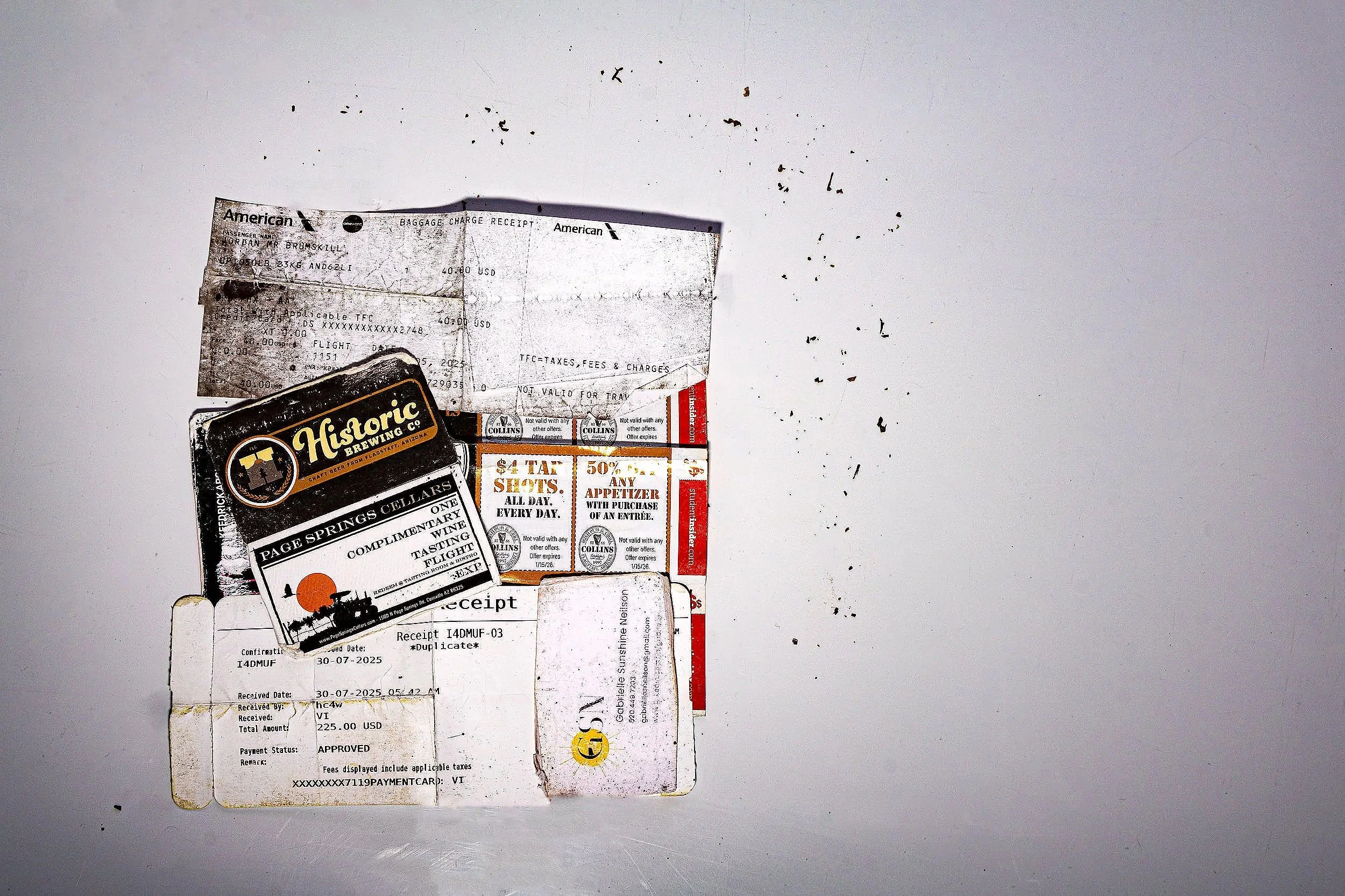 Collection of airline baggage receipts and promotional flyers on a white surface, some damaged and stained.