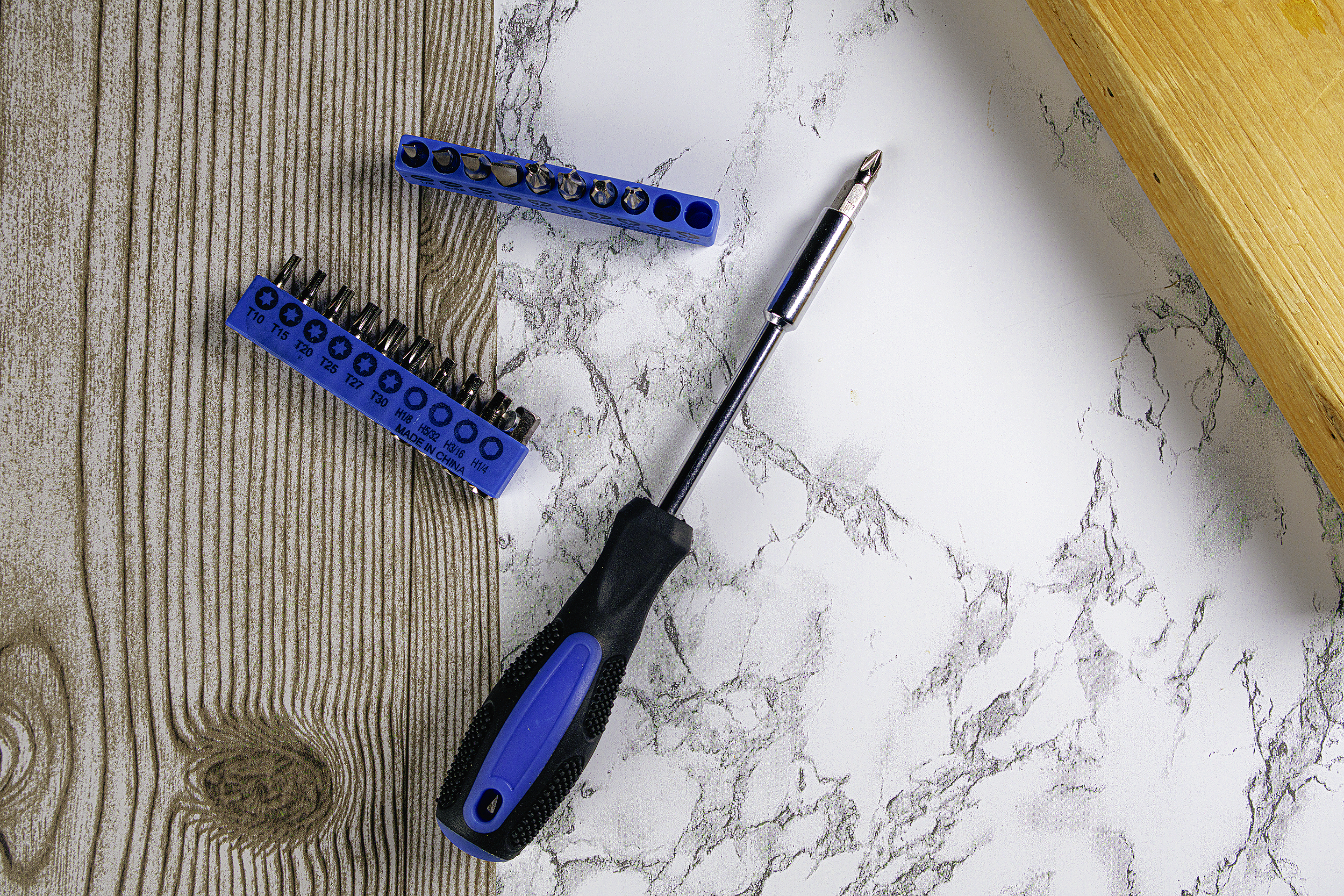 A screwdriver, a set of screwdriver bits, and two blue bit holders on a surface with a wood and marble pattern.