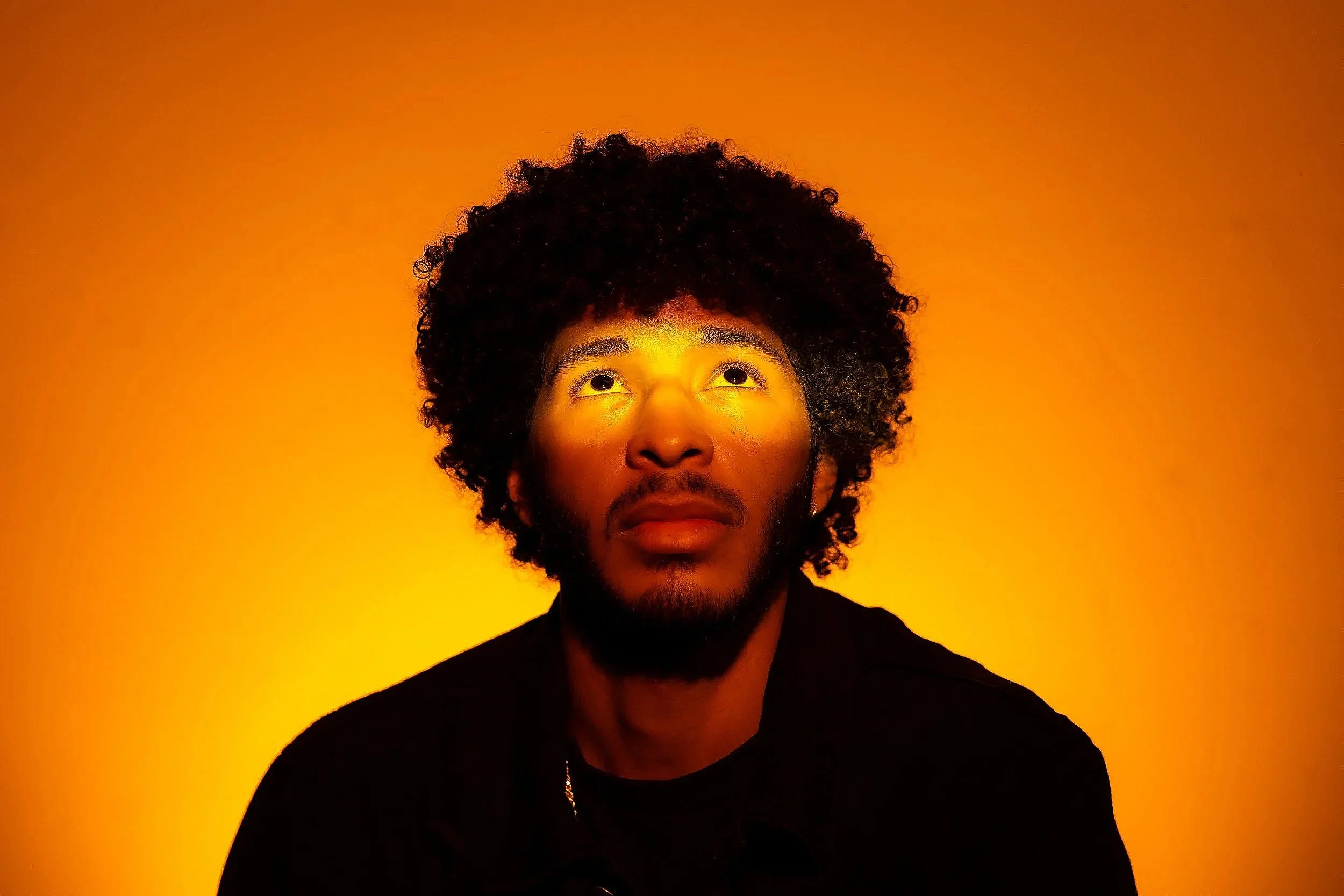 Portrait of a man with curly hair and a beard against an orange background.