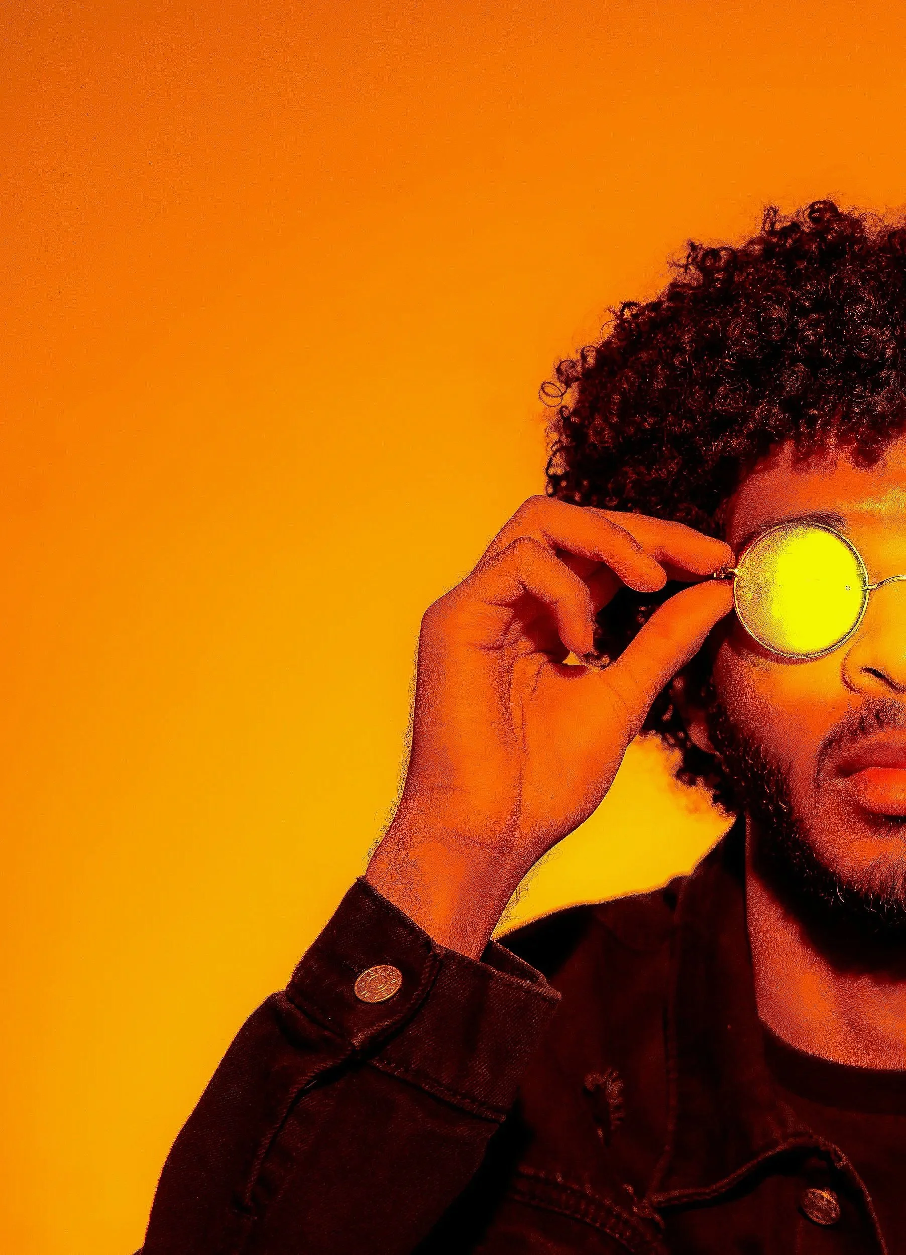 A person with curly hair holding a round yellow object to their face, against an orange background.