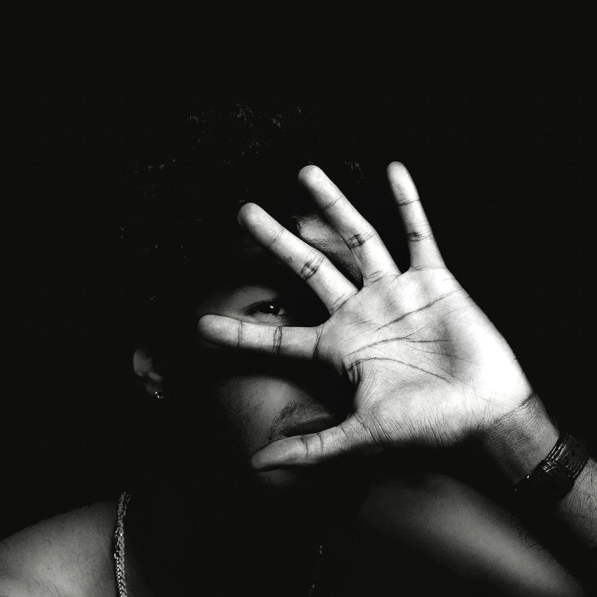 Black and white photo of a hand with fingers spread, showing a chain of small beads hanging down towards the bottom of the image.