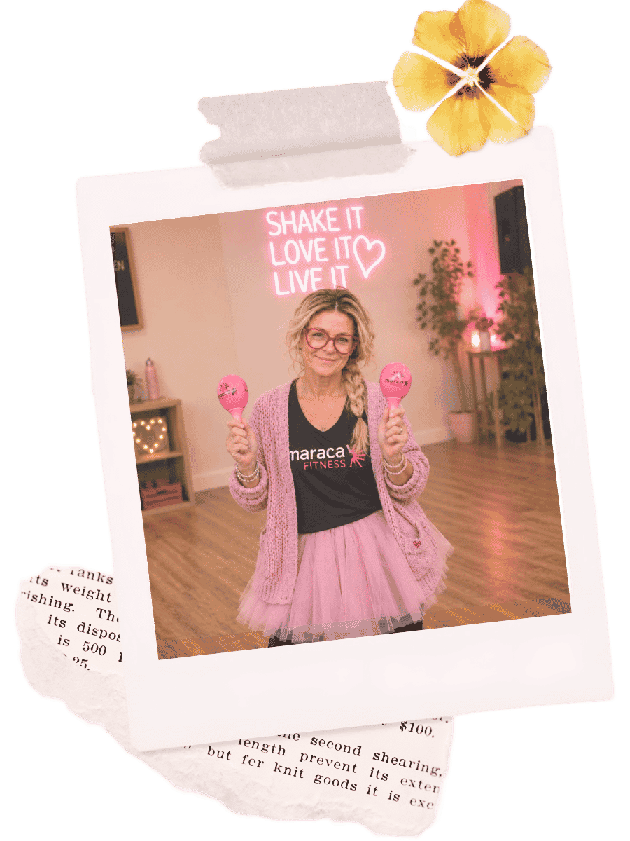 Helena with blonde wig in a braid, wearing glasses, a bright pink neon sign behind her that reads 'SHAKE IT LOVE IT LIVE IT,'.