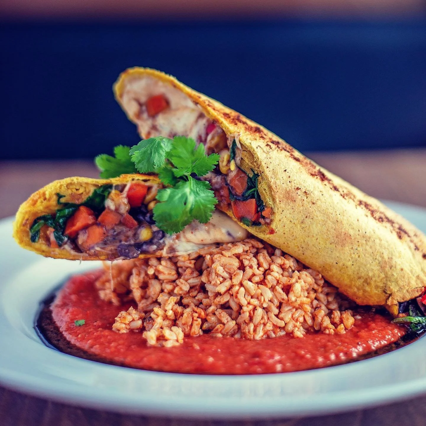 Atlas Classic: Enchiladas: Black beans, roasted corn, yams, bell peppers, greens & mozzarella cheese, baked in a tortilla, served with tomato sauce, chipotle sour cream & dirty rice.