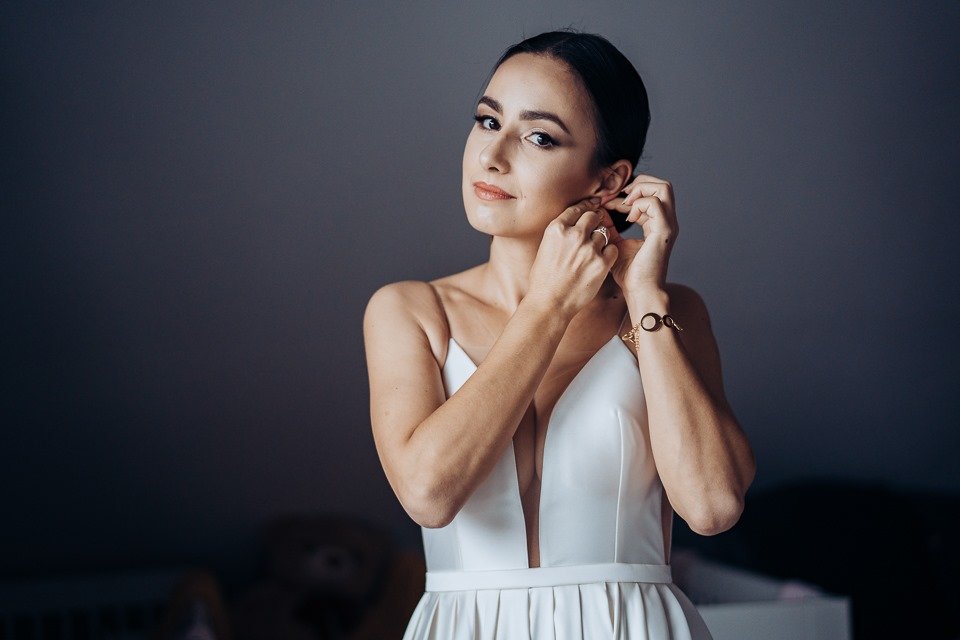 Elegantes Porträt einer Frau in einem weissen Kleid vor dunklem Hintergrund, aufgenommen in einem ruhigen Studio-Look.