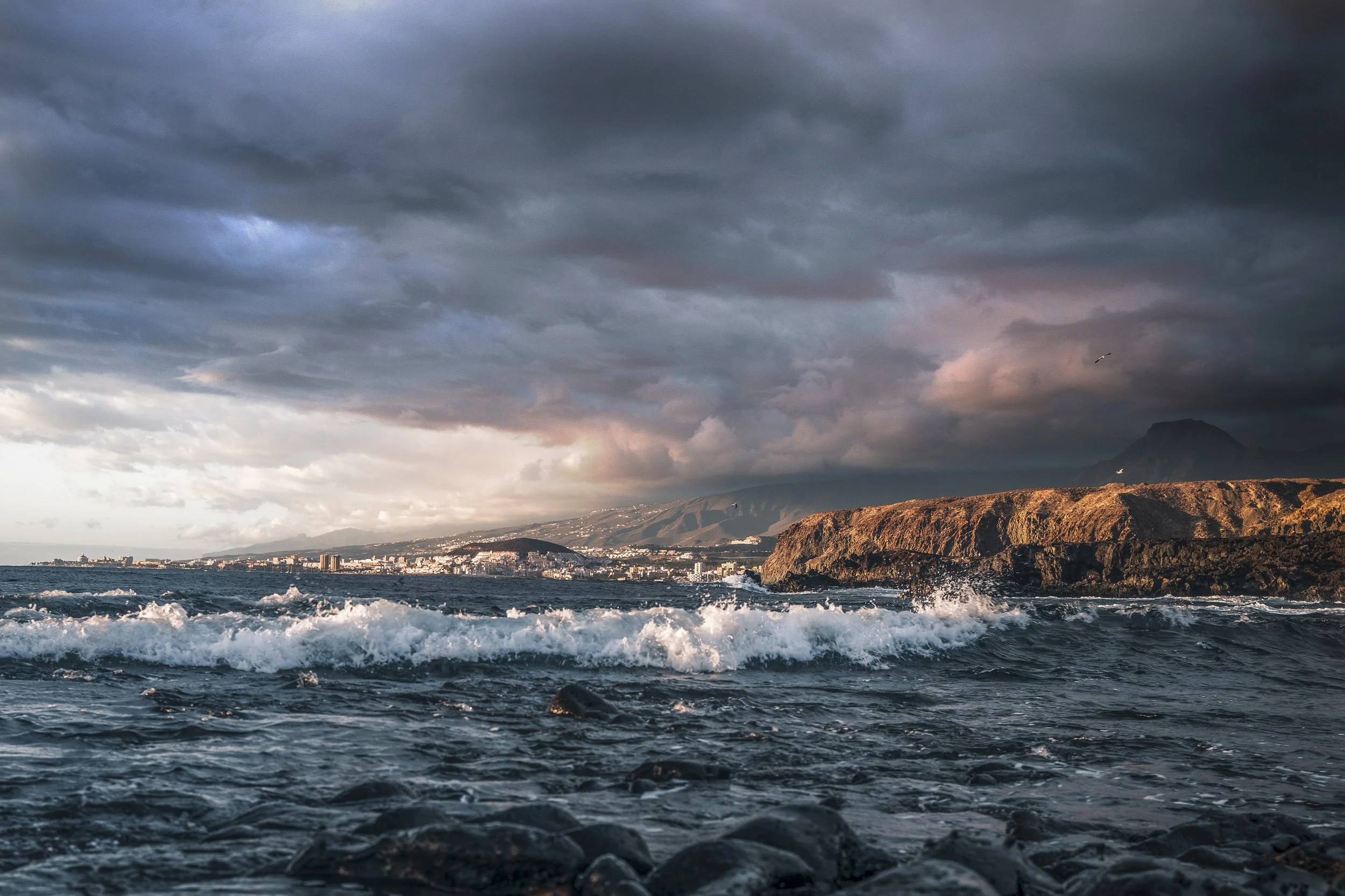 Dramatisches Landschaftsfoto mit Meer, Bergen und Wolken bei stimmungsvoller Abendstimmung.