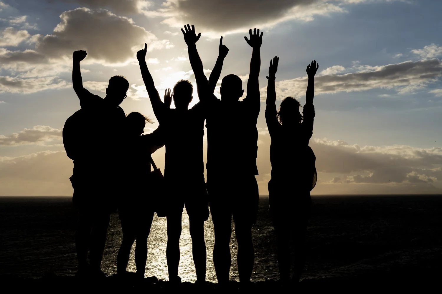 Stimmungsvolles Gruppenfoto bei Sonnenuntergang, mit Silhouetten von Menschen in einer fröhlichen und lebendigen Atmosphäre.