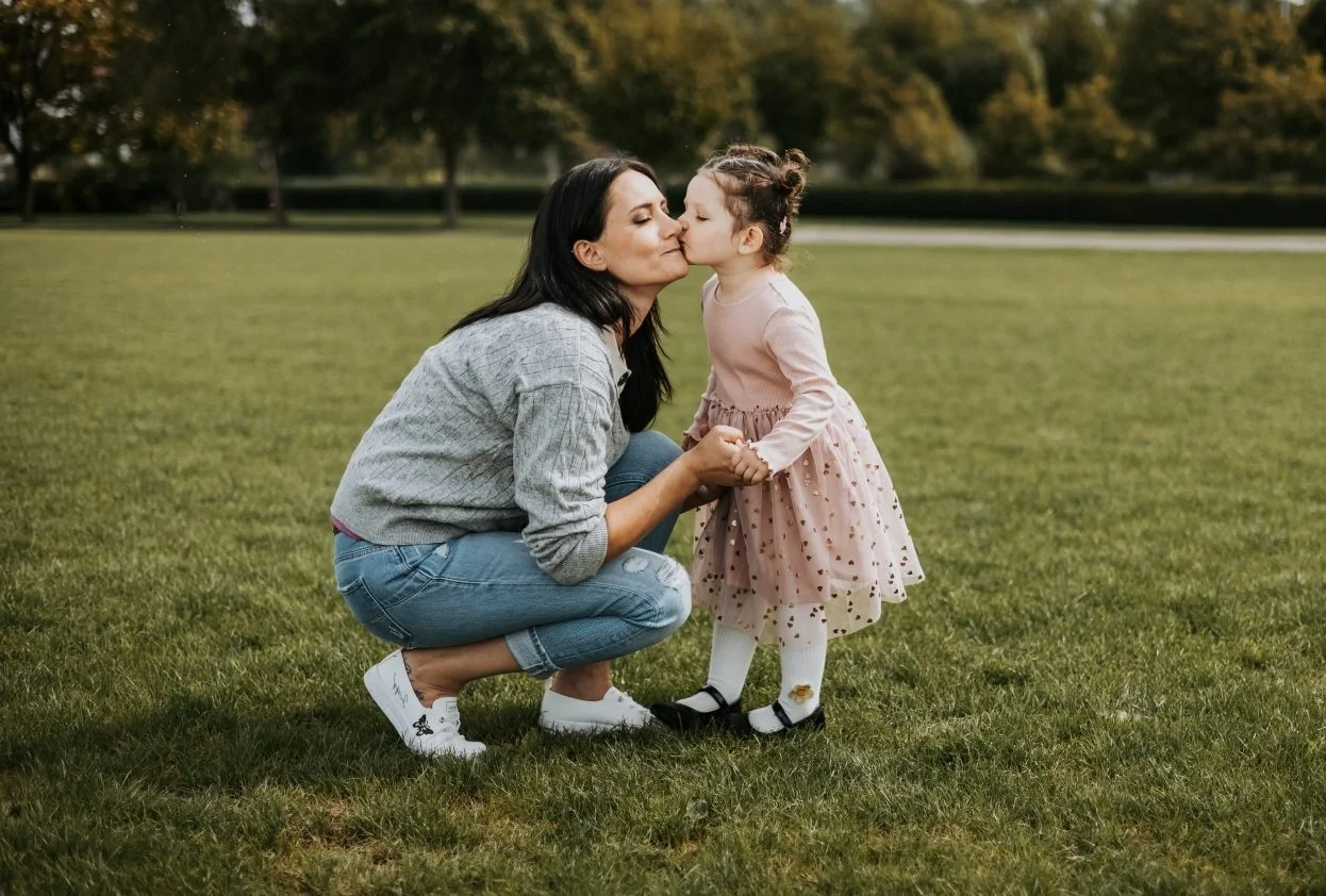 Natürliches Familienfoto von Mutter und Kind auf einer Wiese im Park, festgehalten in einem liebevollen Moment.