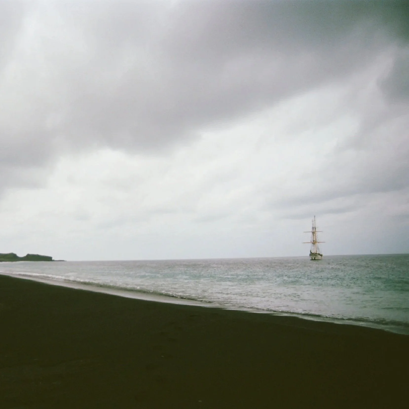 A large body of water with a ship sailing in the distance under a cloudy sky.