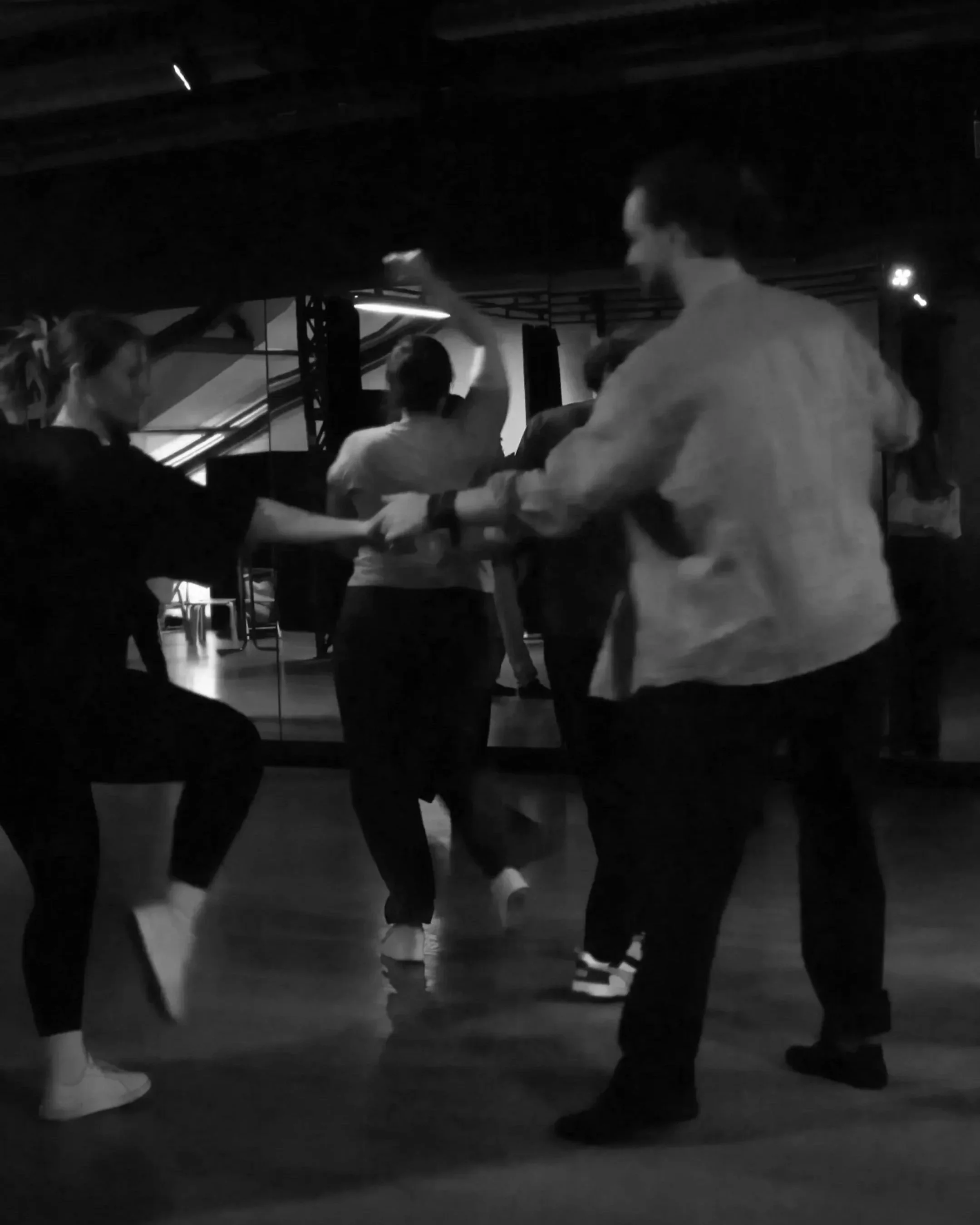 People dancing in a dark room, forming a circle, with one person in the middle holding a microphone.
