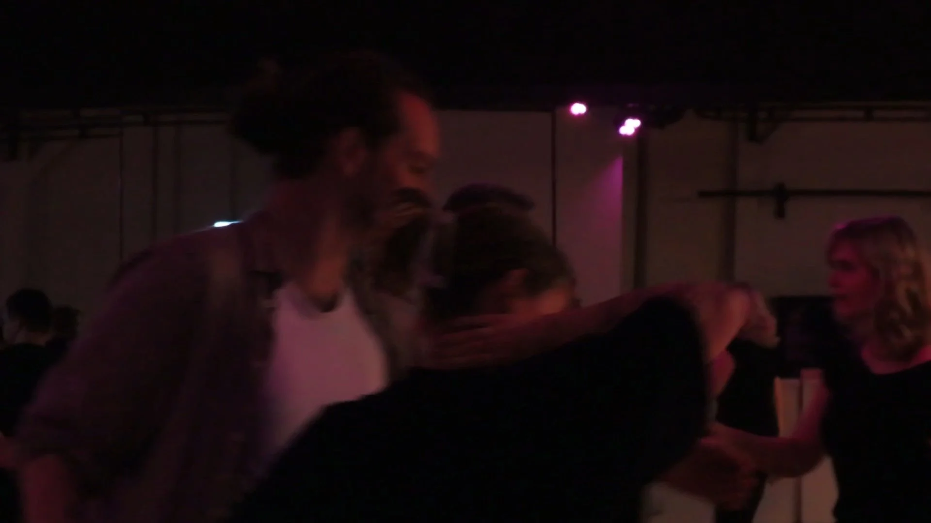 People dancing in a dimly lit room with purple and pink stage lights.