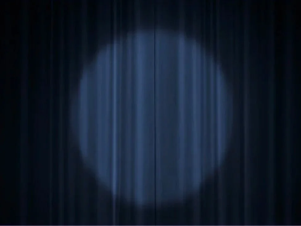 A dark theater curtain with a faintly illuminated circle in the center.