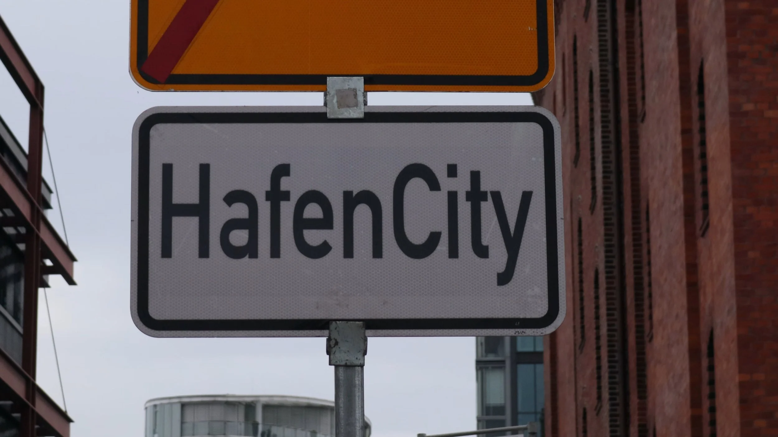 Street sign indicating the entrance to HaeN City, with buildings and overcast sky in the background.