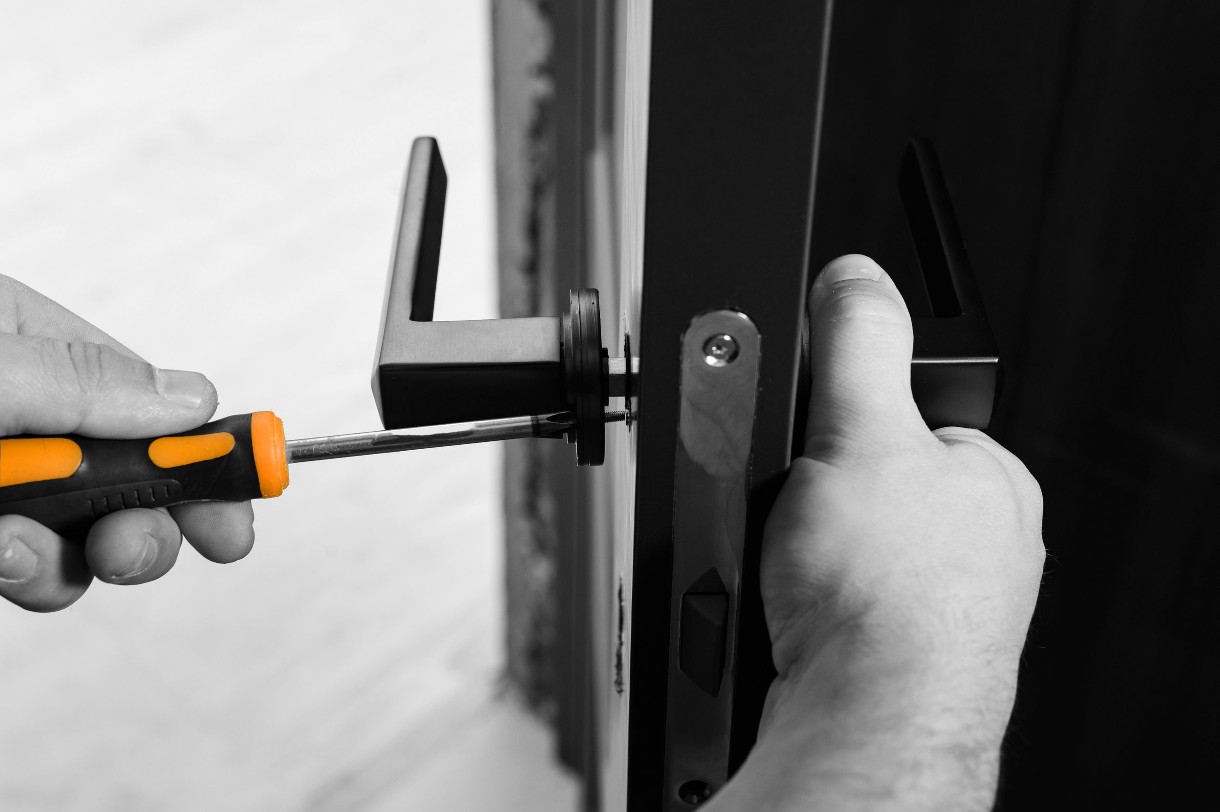 Black and white close-up of a person's hands using a screwdriver to tighten a screw on a metal or electronic device.