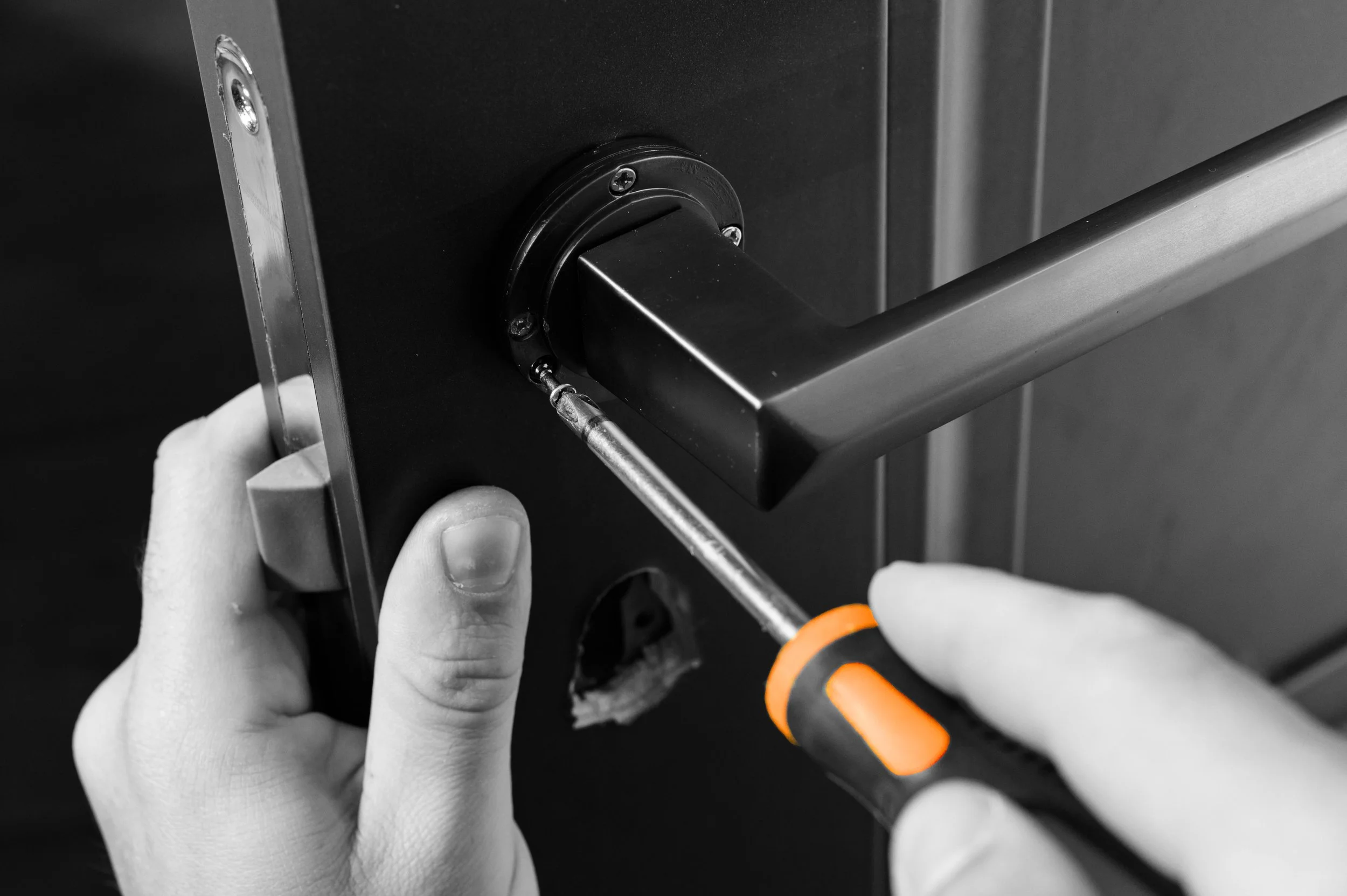 A person using a screwdriver to attach a circular component to a black metallic surface, with their fingers visible.