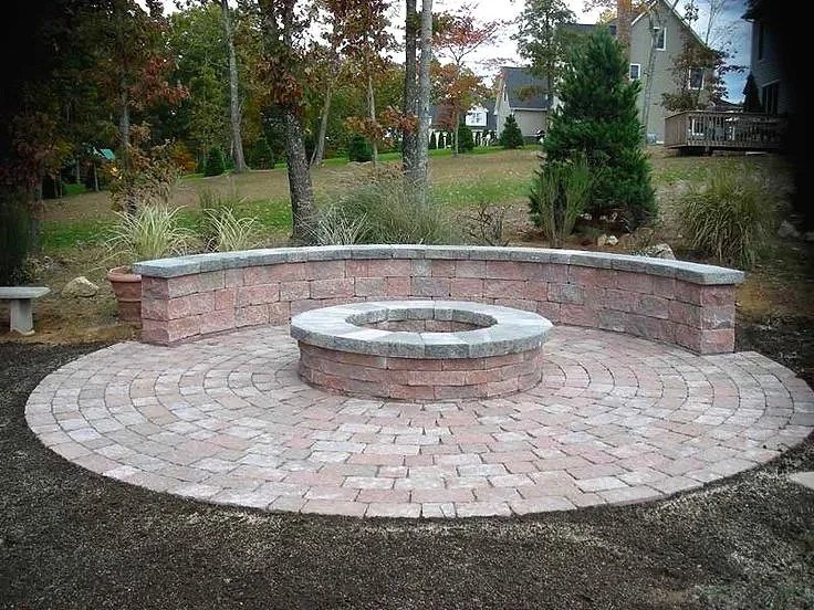 Circular brick fire pit and curved seating wall installed in a landscaped backyard patio area.